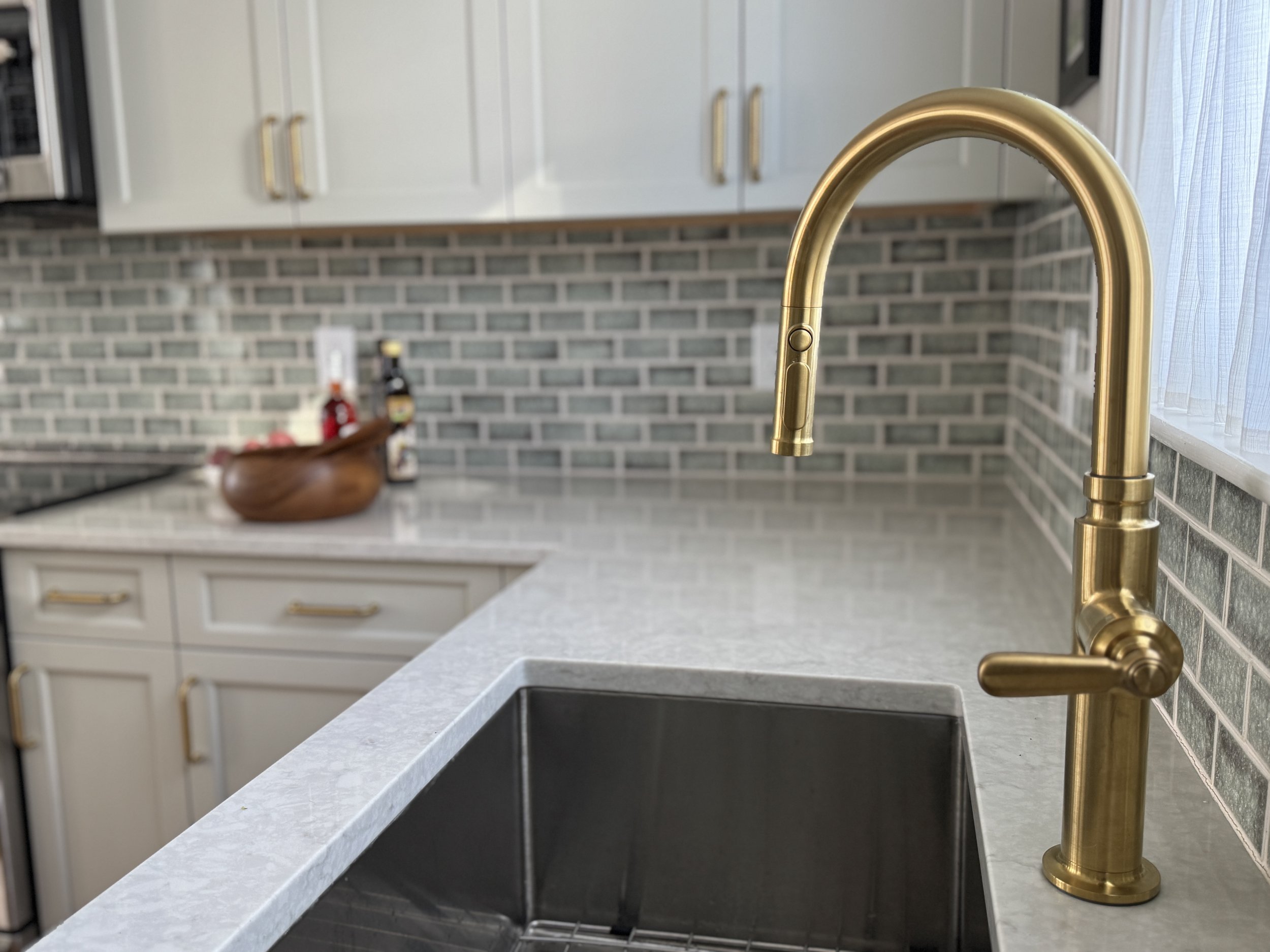 Kitchen detail with brass faucet, green tile backsplash, and countertop showing material relationship