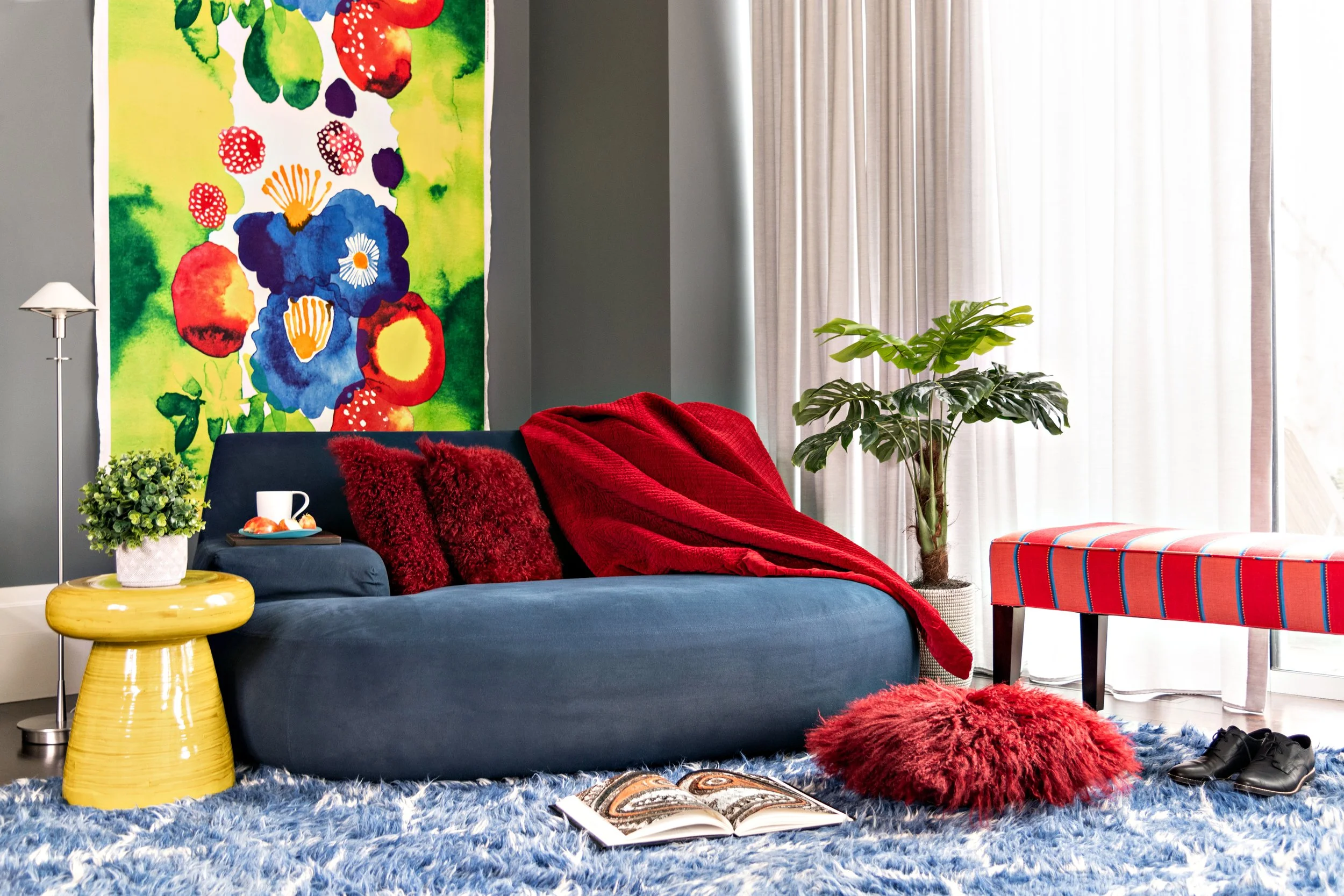 Lincoln office lounge with deep blue chaise, red pillows, Marimekko floral textile, custom red-striped ottoman, cobalt Beni Ourain rug, and yellow mushroom-shaped wood side table.