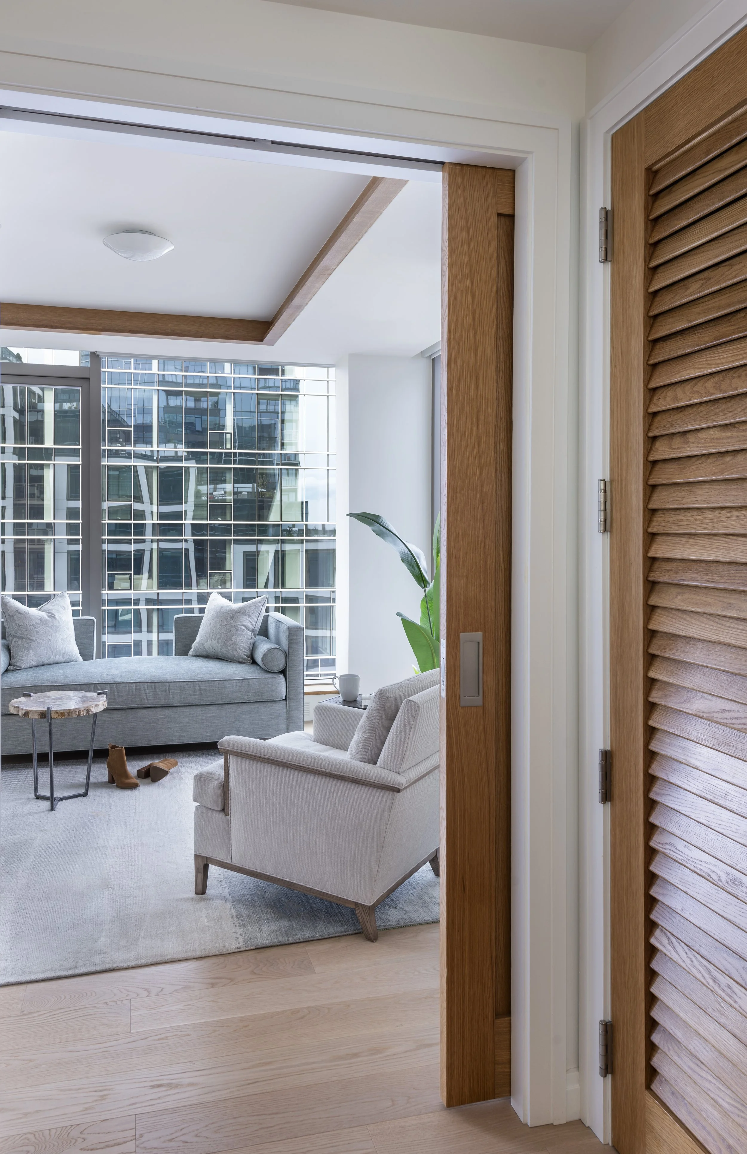 Seaport sitting room with blue chaise lounge, silk rug, ivory accent chair, live-edge wood side table, rift oak floors, and floor-to-ceiling windows.
