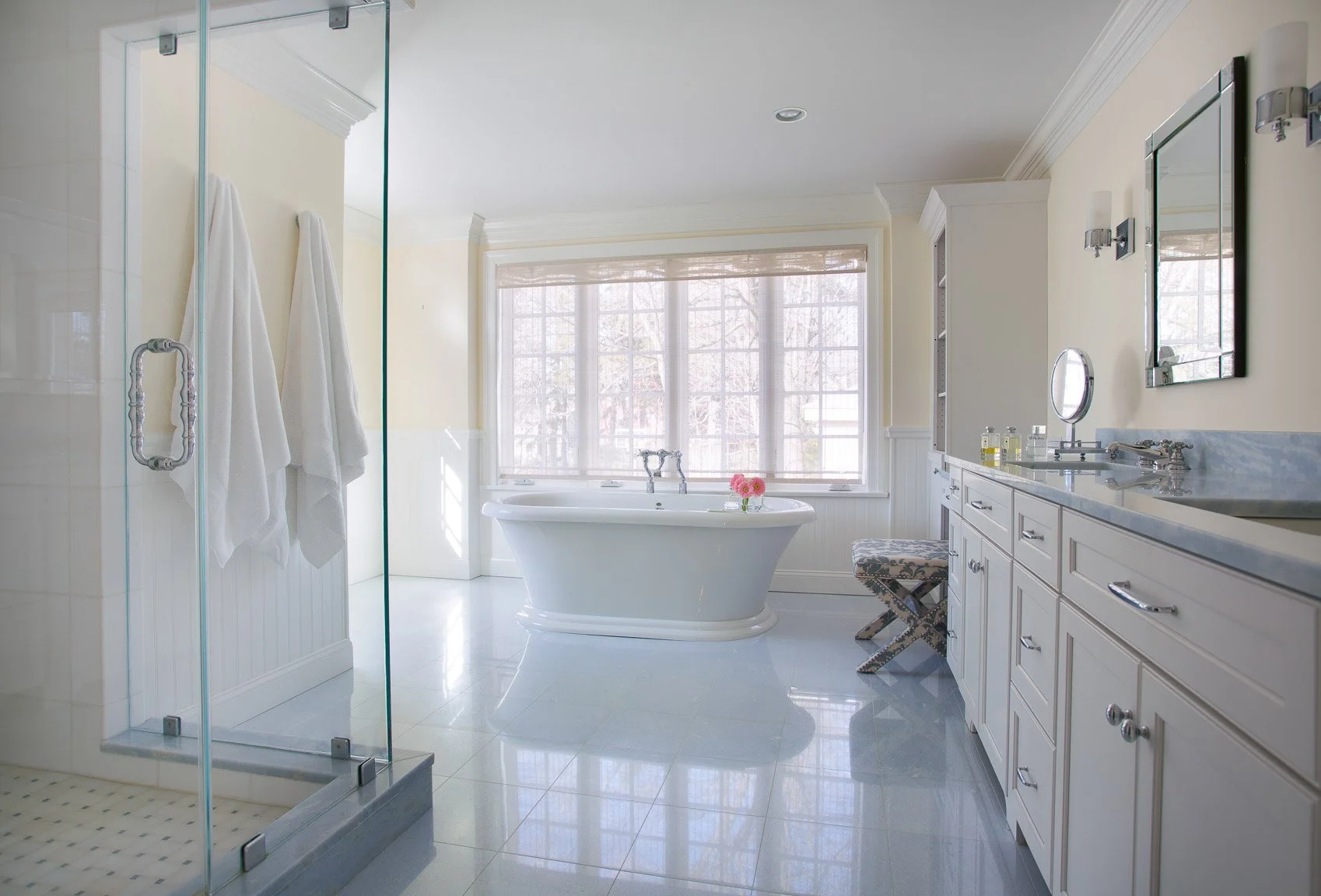 West Newton primary bathroom with freestanding tub, large windows, glass shower, white cabinetry, Lagos Azul counters and tile flooring.