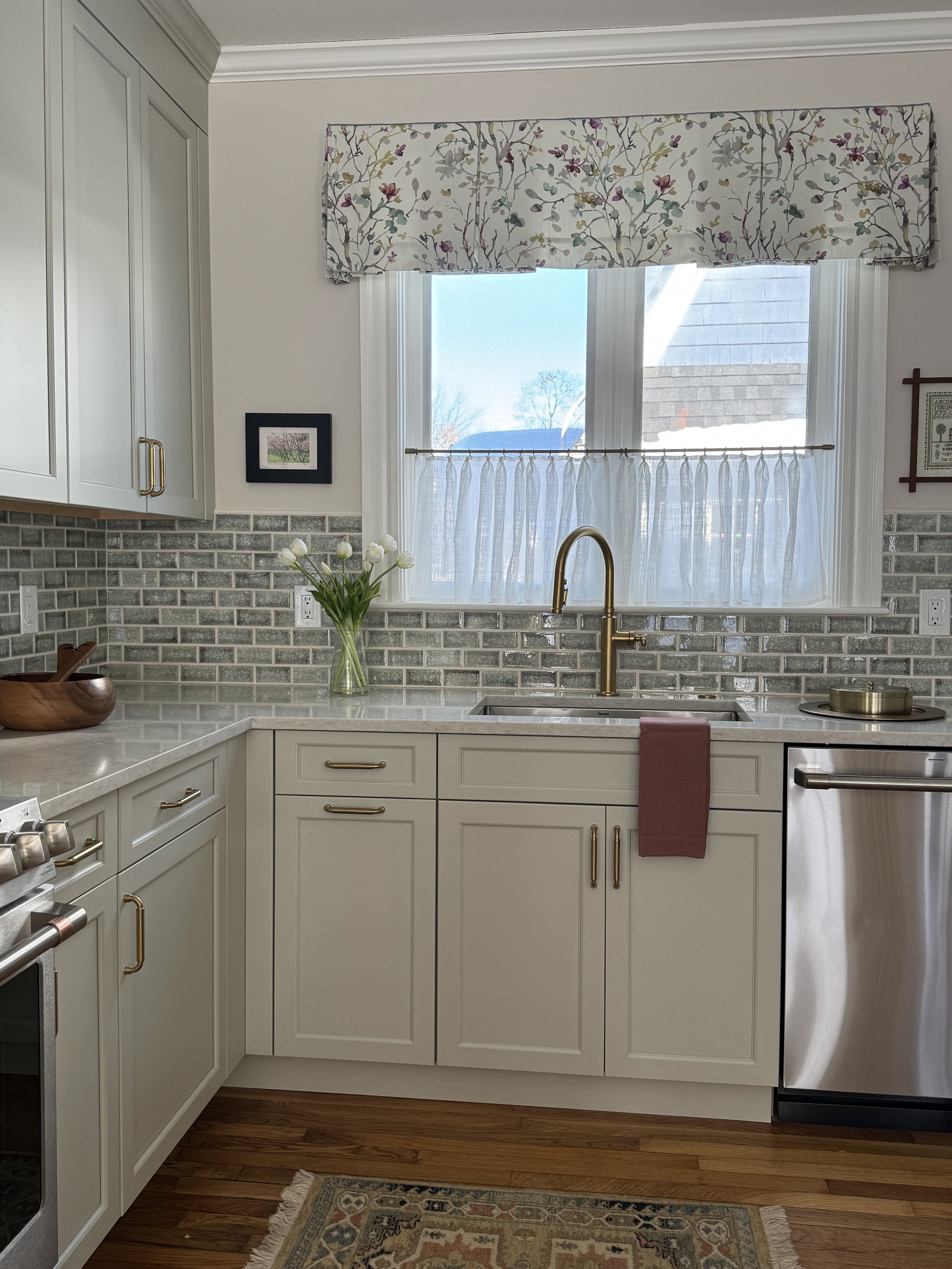 Kitchen with pale green cabinets, green tile backsplash, valance and sheer at window, and improved storage and layout