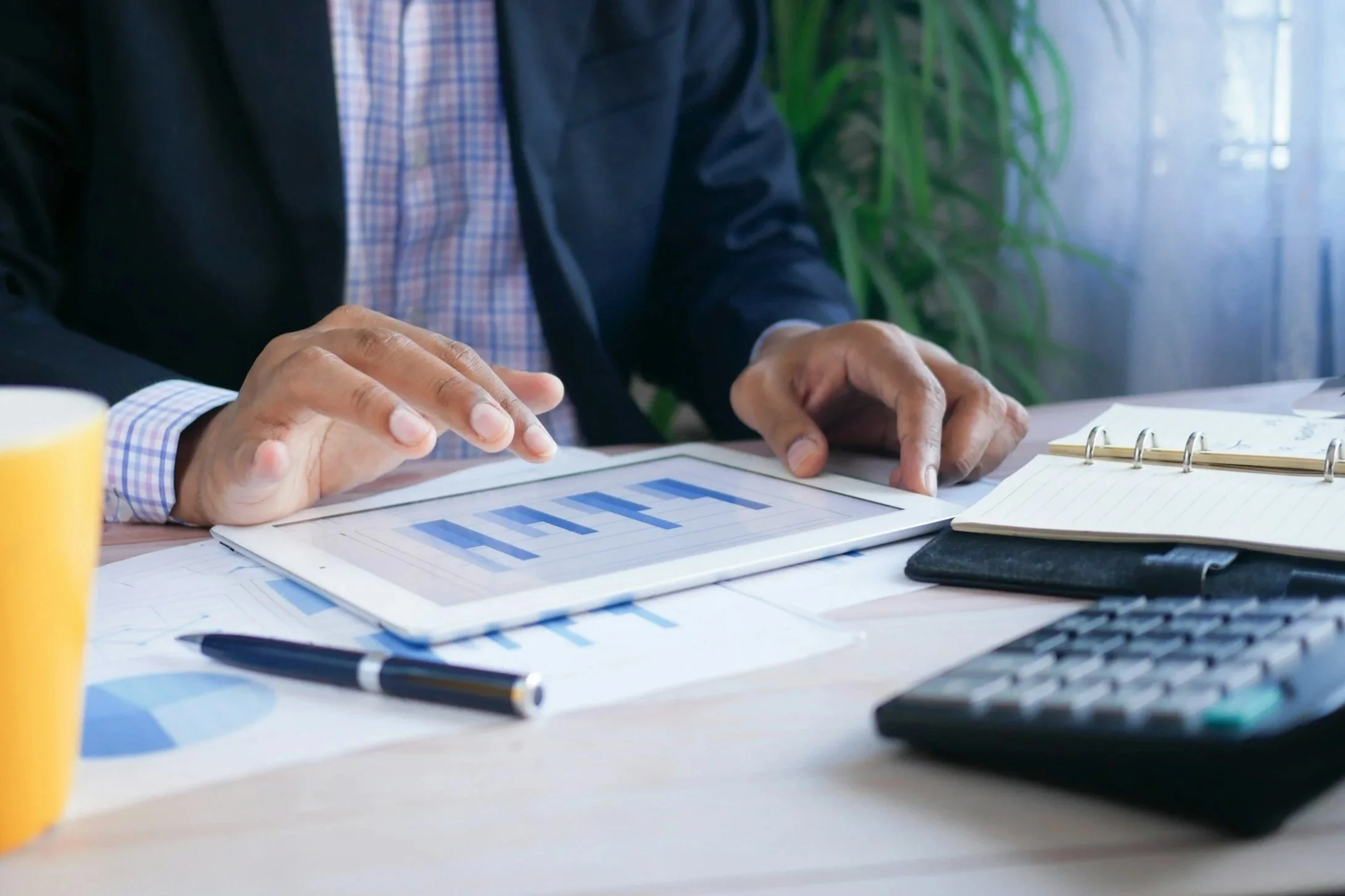 Financial portfolio review - A person in a business suit sitting at a desk, reviewing graphs and documents, with a pen and notepad on the desk.