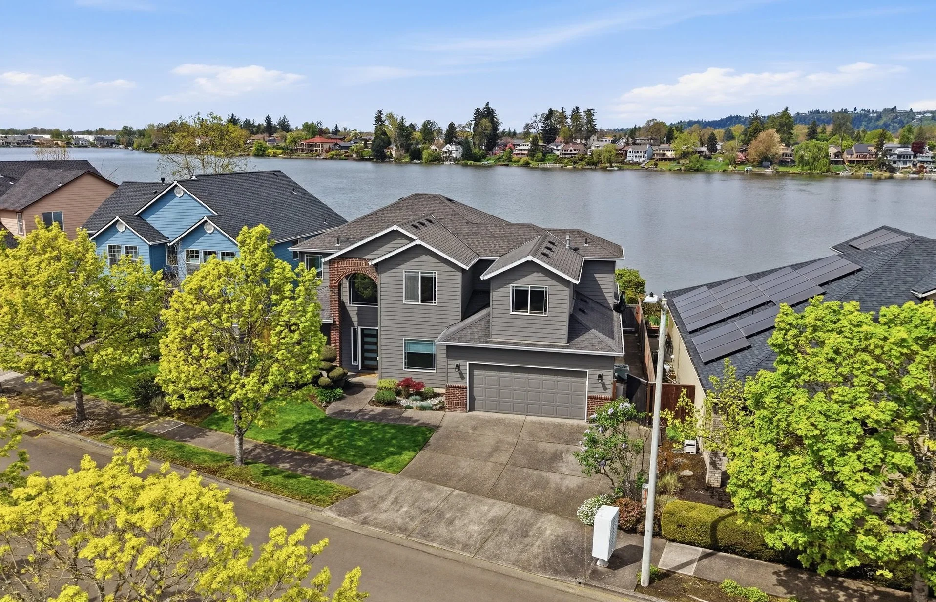 Aerial view of residential neighborhood with houses by a lake, lush green trees, and a partly cloudy sky.