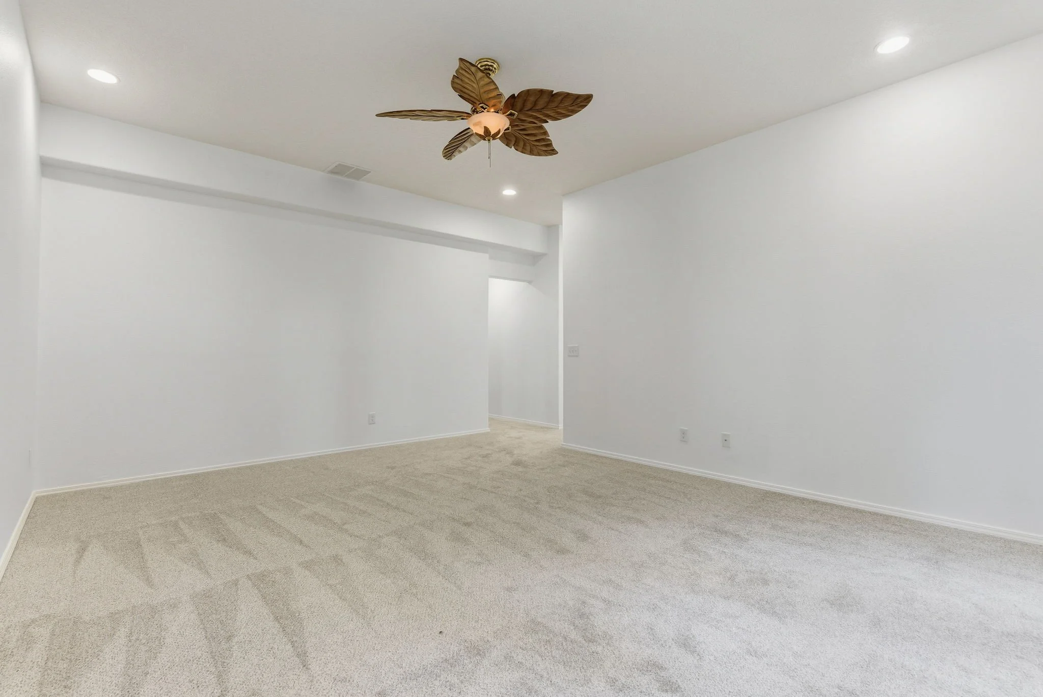 Empty room with white walls, beige carpet, a ceiling fan with leaf-shaped blades, and recessed lighting fixtures.