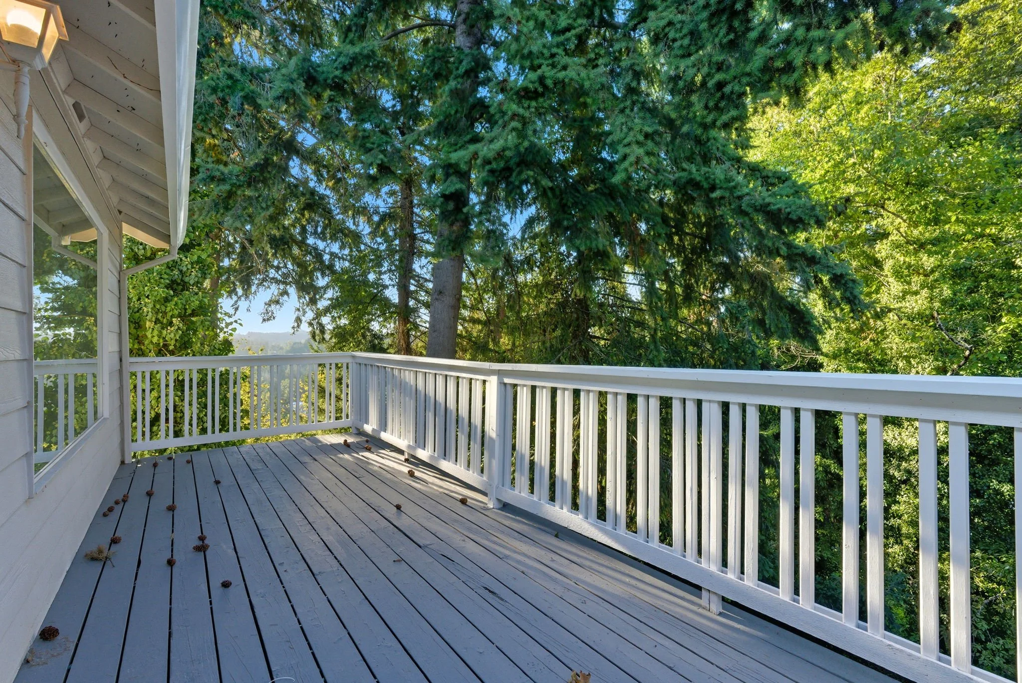A wooden balcony with white railings overlooking a lush green tree canopy on a sunny day.