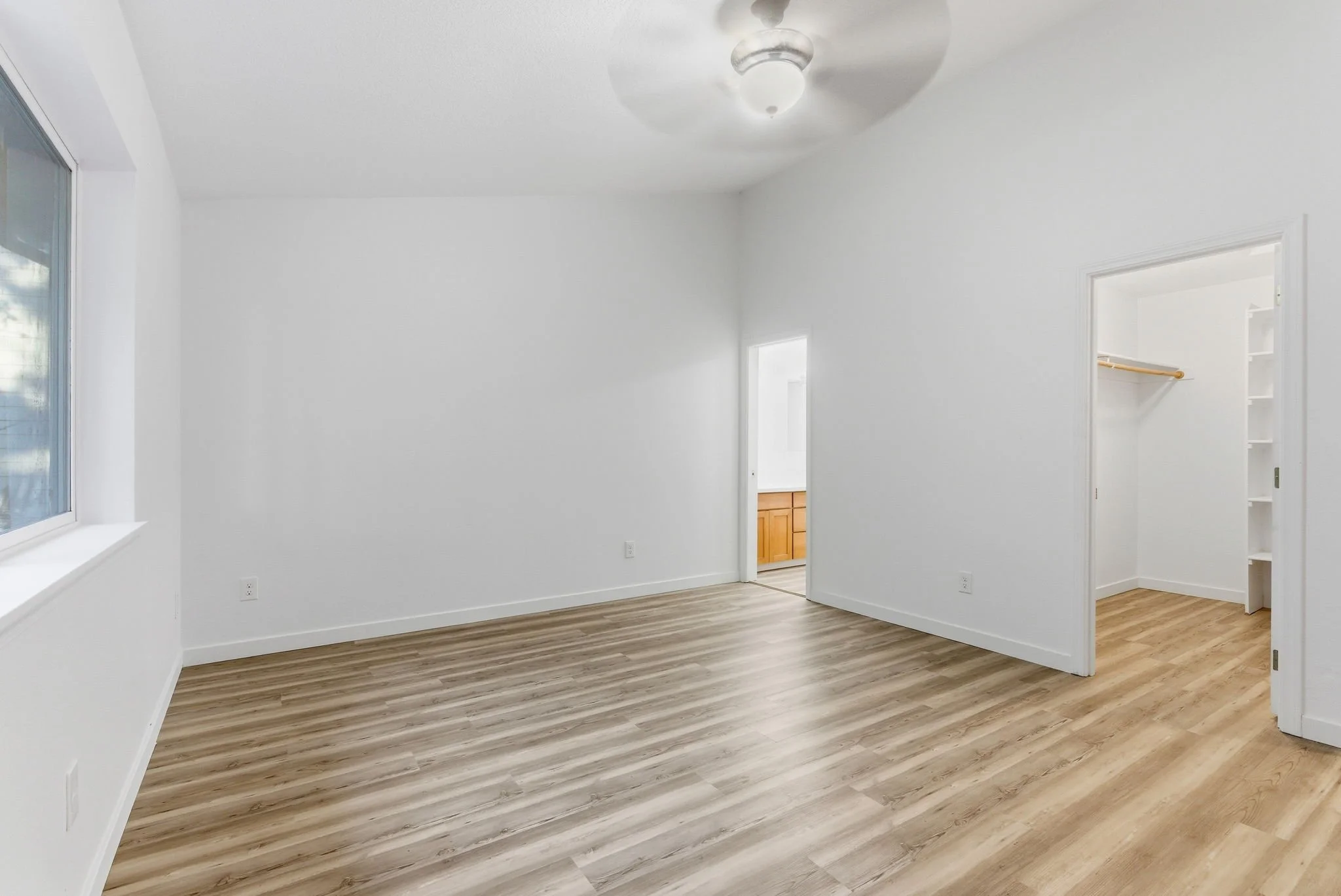 Empty room with white walls, a window on the left, a ceiling fan, and an entry to a walk-in closet with built-in shelves on the right.