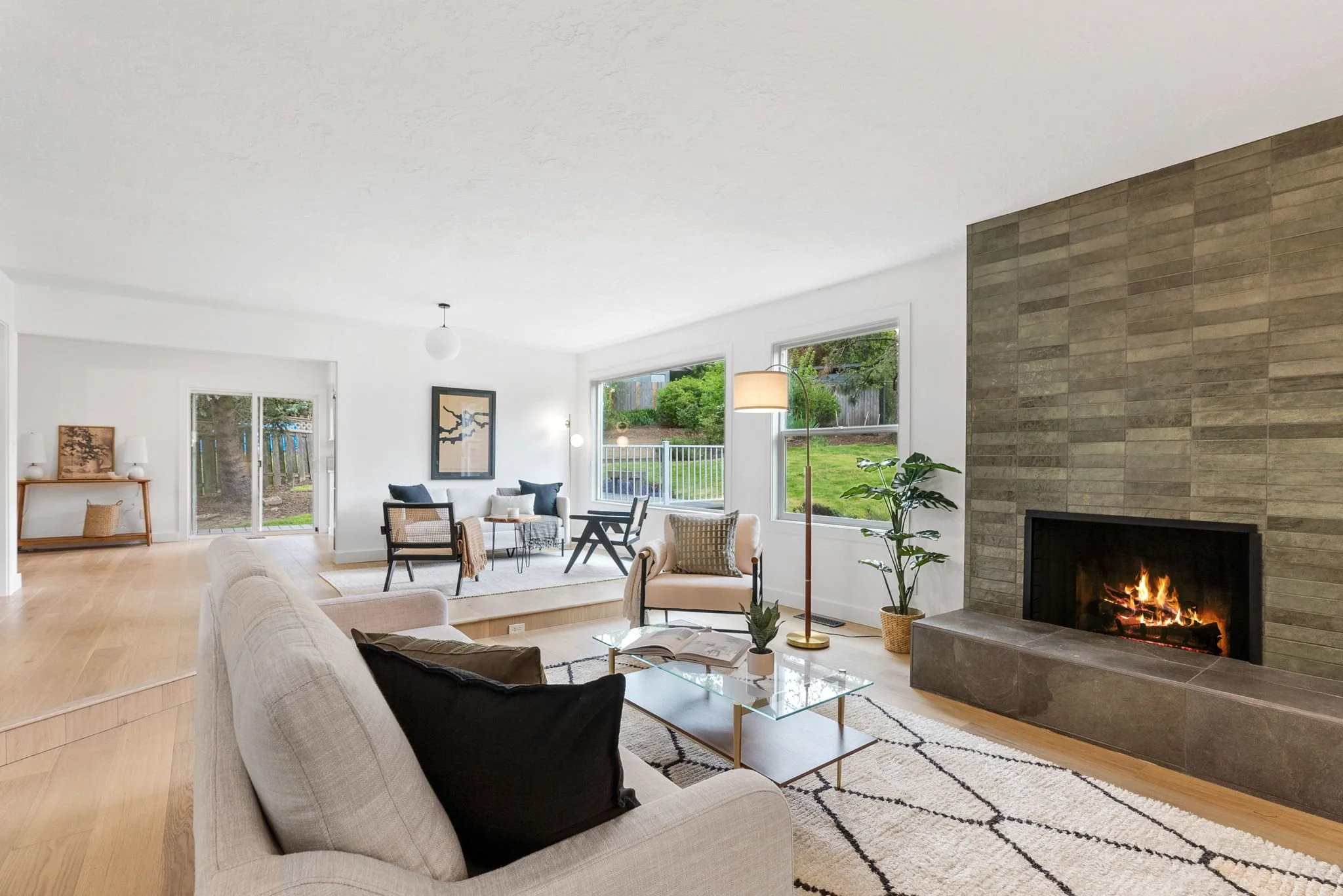 Living room with beige and black furniture, a fireplace, large windows, and a view of a backyard.