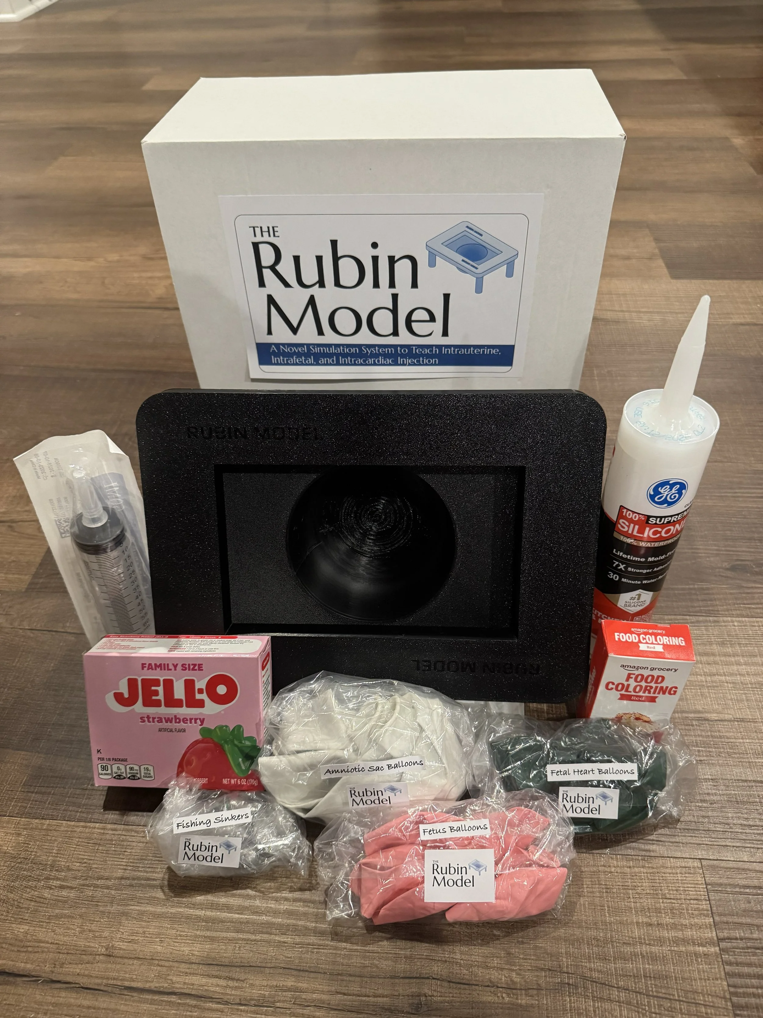 Educational kit for practicing intrauterine, intrafetal, and intracardiac injections, including a model, silicone mold, balloons, food coloring, syringe, and packaging.