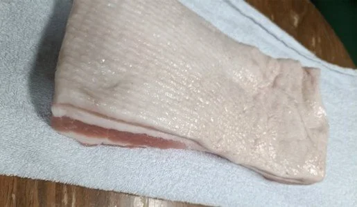 A wedge of pork belly on a cutting board.