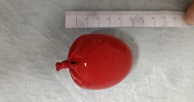 A red, balloon-shaped object placed on a light-colored surface with a ruler showing its size.