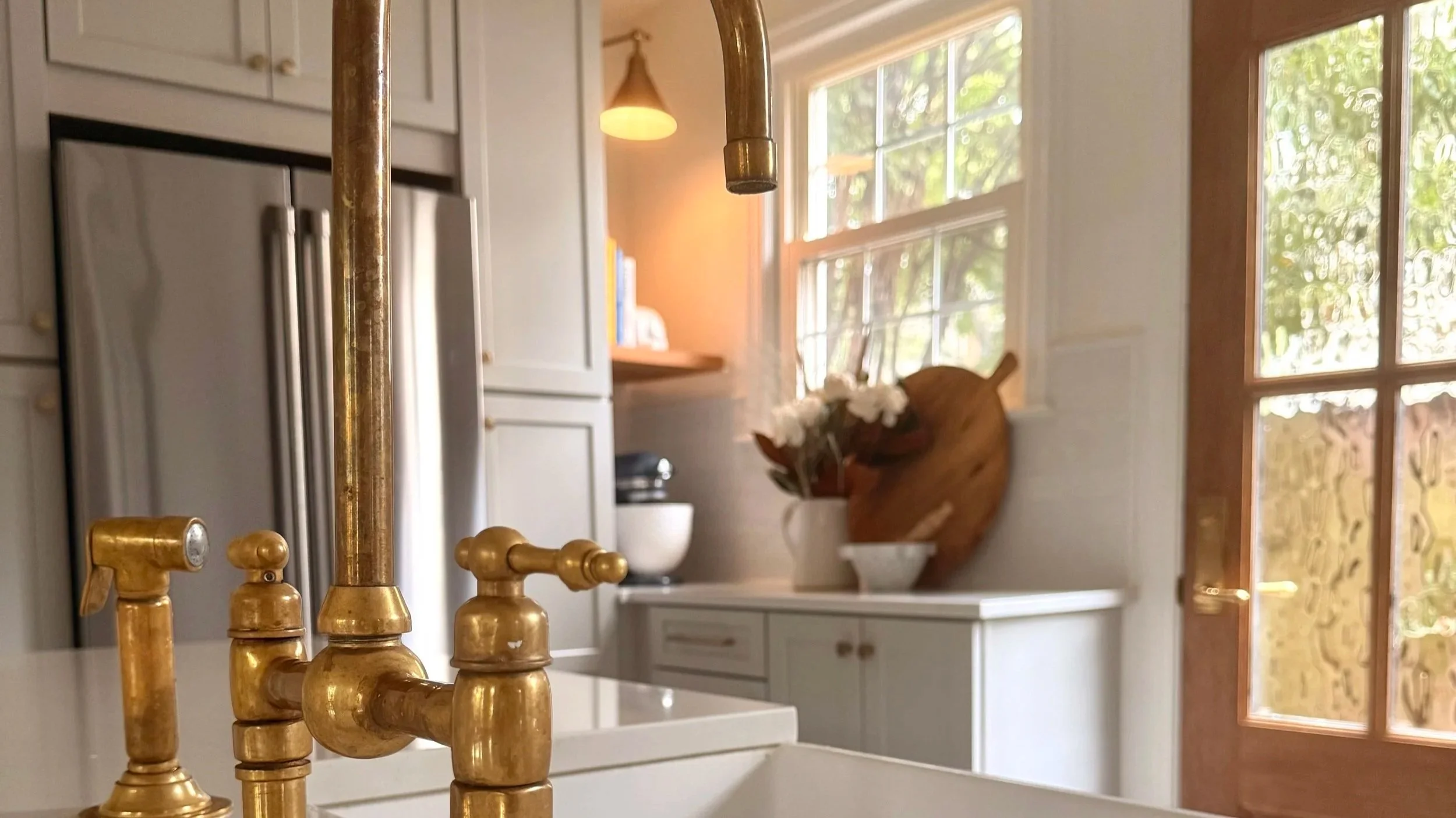 A kitchen countertop with a large floral arrangement of white roses and greenery in a white pitcher, accompanied by a wooden knife holder, small wooden containers and a coffee machine, shows how beautiful detailing can transform everyday living.