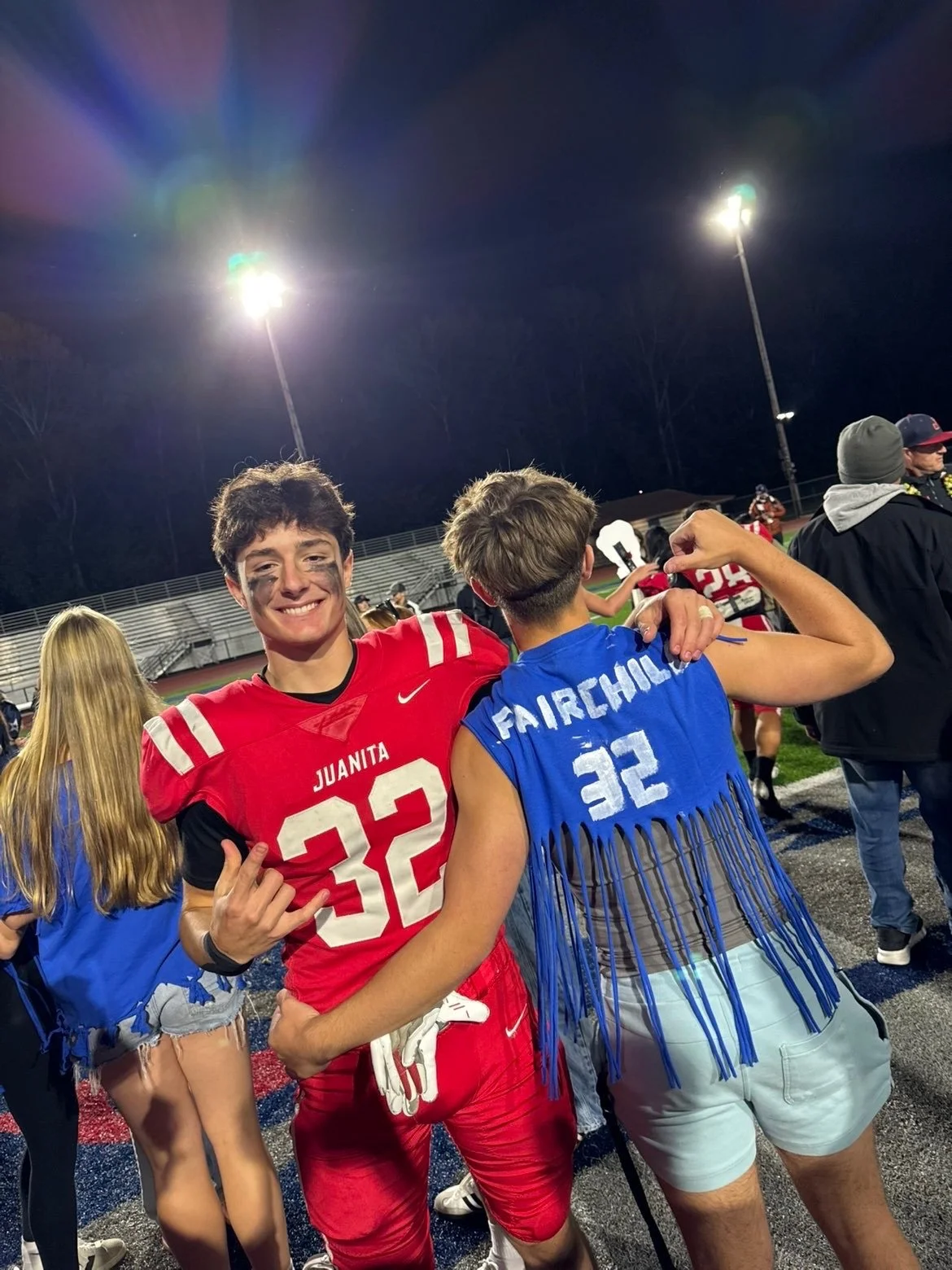 Young man in a black suit and blue tie smiling outdoors in front of a garage.