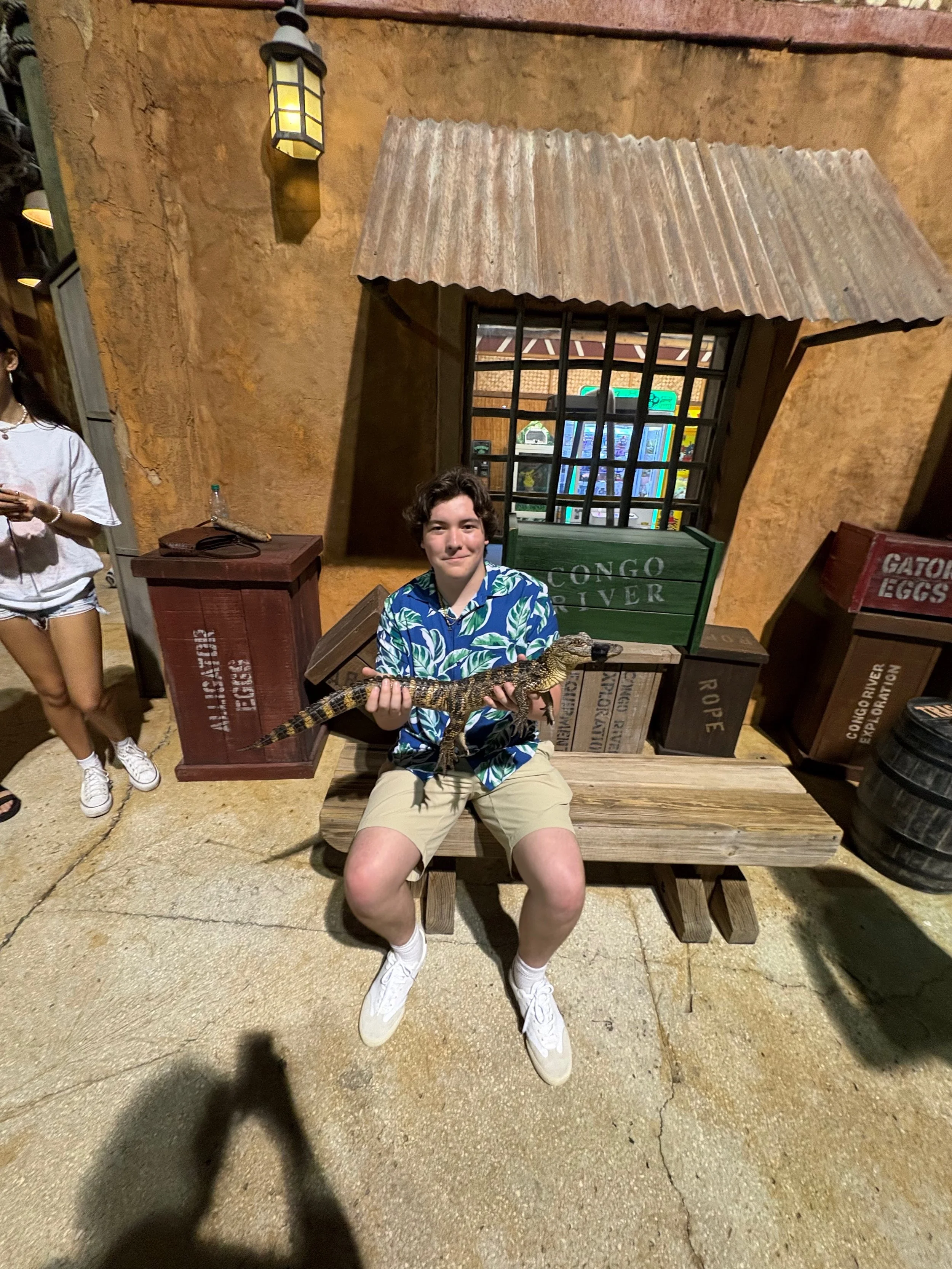 A young man with wavy brown hair sitting by an airplane window, looking outside with a slight smile, wearing a blue hoodie that says 'the future is here' with a yellow and black logo for '20 broken planet'.
