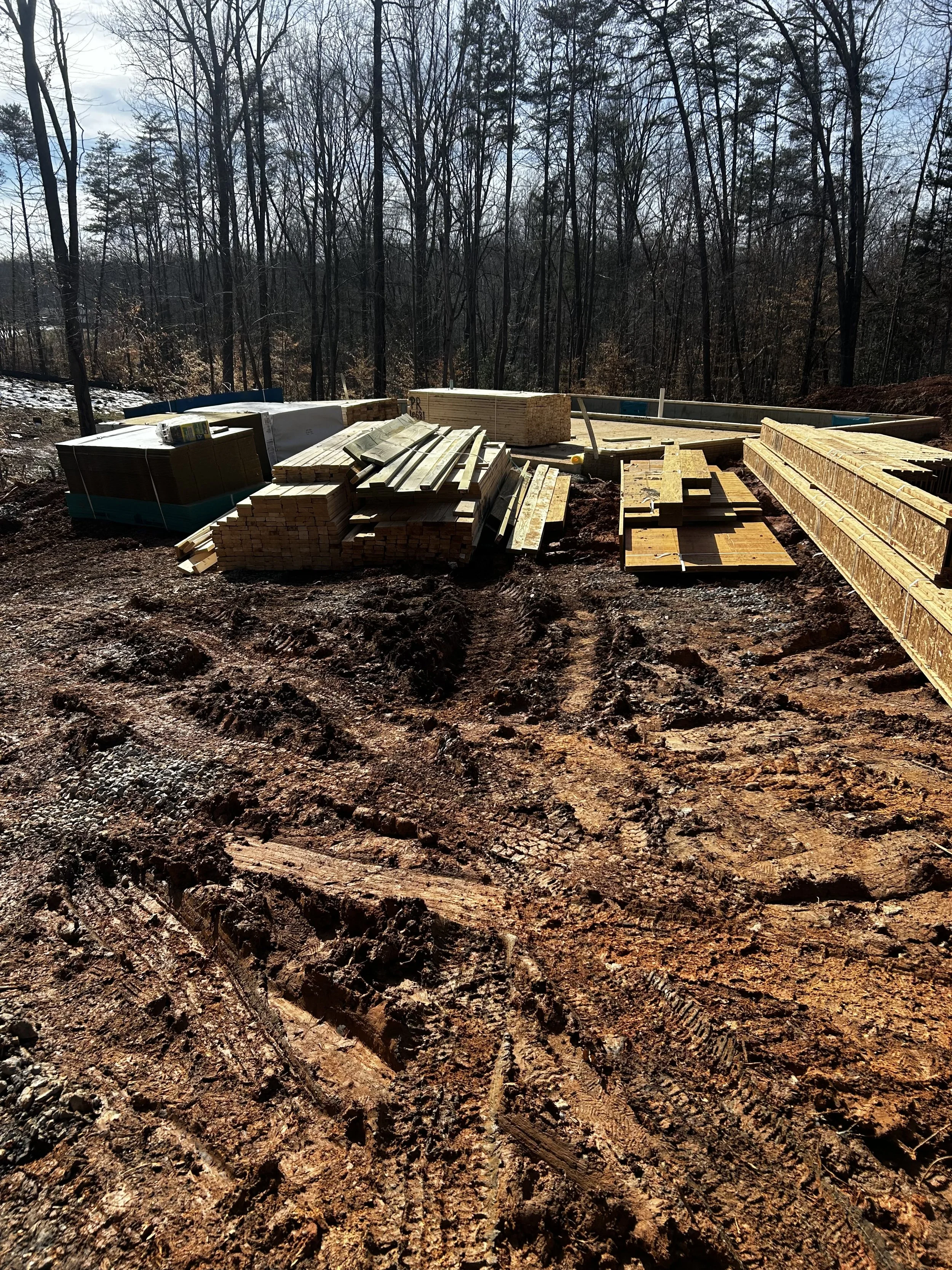 First lumber drop for the R&W Homes Erica model custom home at 10631 Plank Road in Spotsylvania VA with foundation walls visible and framing materials staged on site