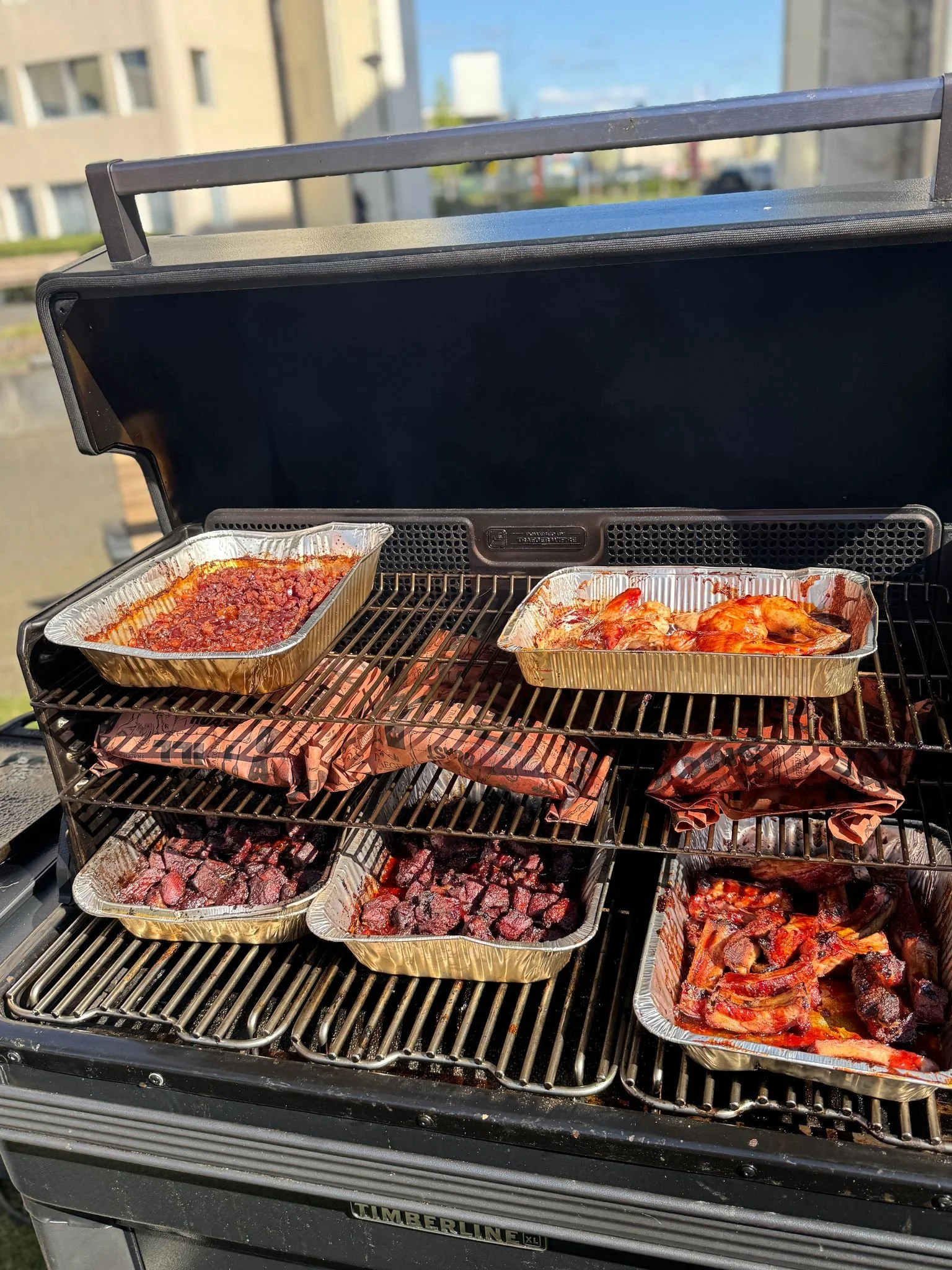 Barbecue met verschillende metalen bakjes met vlees en saus op de grill.