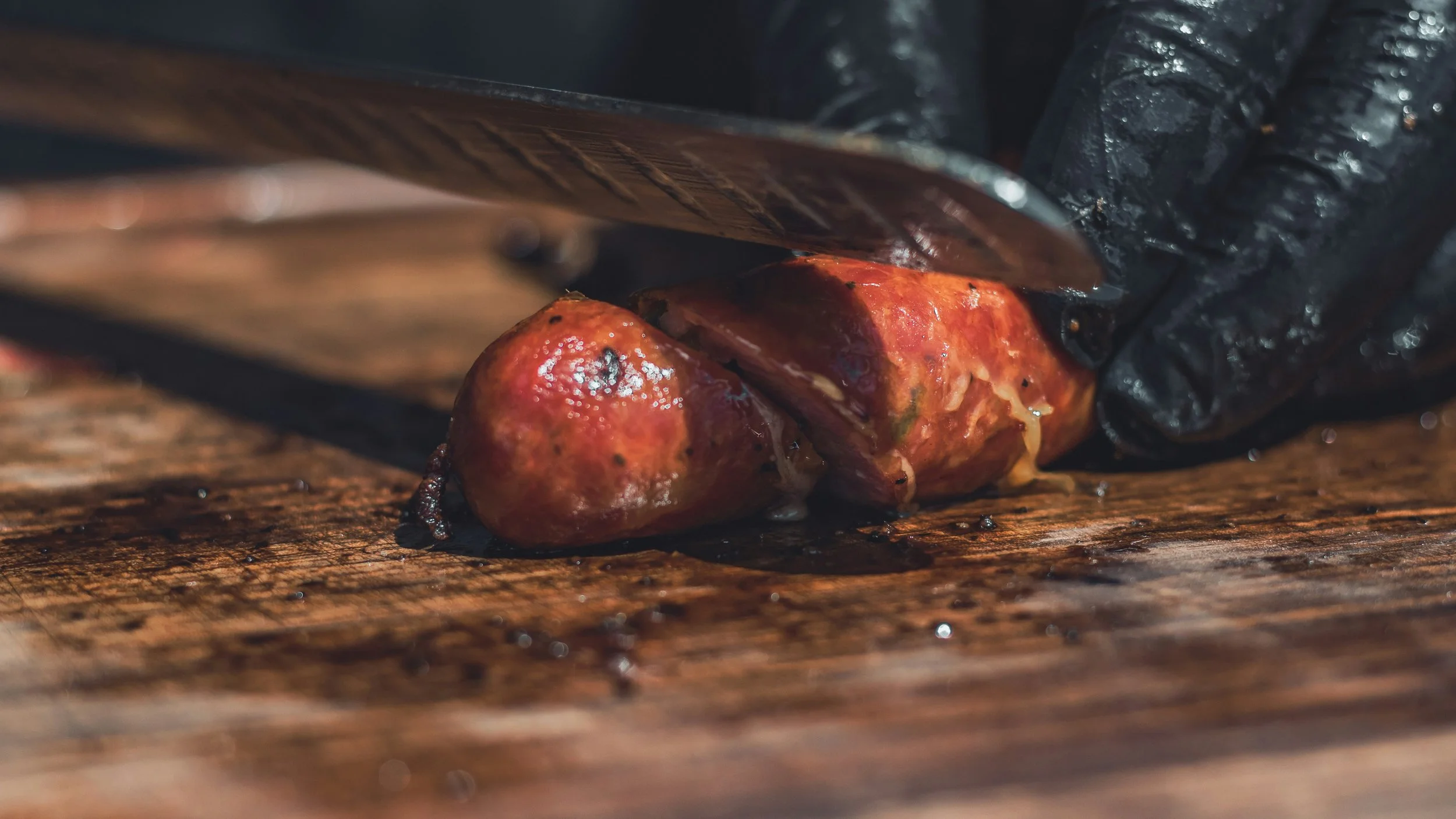 Close-up of a person slicing roasted tomatoes on a wooden cutting board with a knife, wearing black gloves.