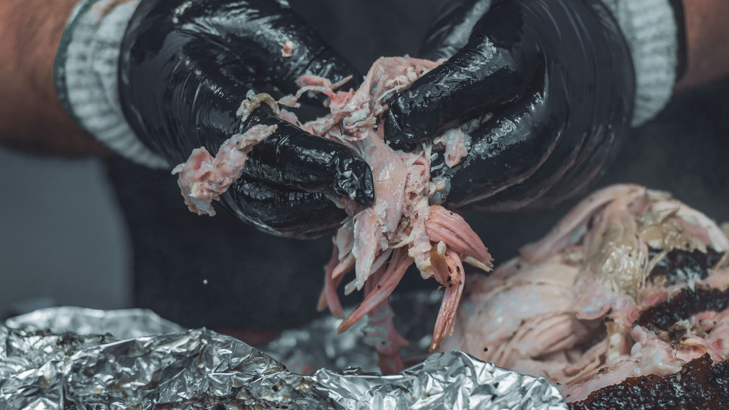 Person wearing black gloves tearing cooked chicken meat over foil