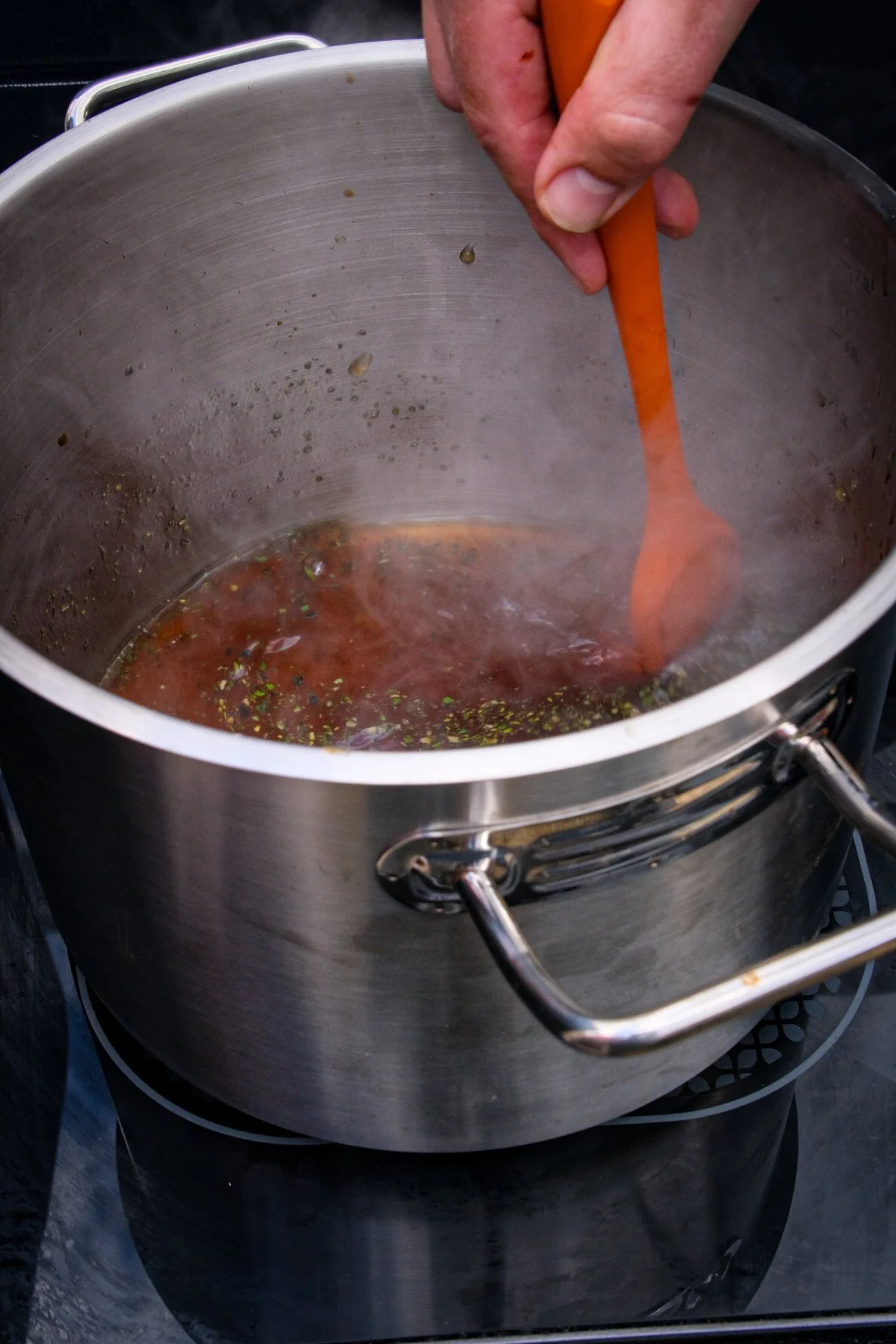 Een hand roert in een grote stalen kookpot die op een elektrisch kookplaat staat.