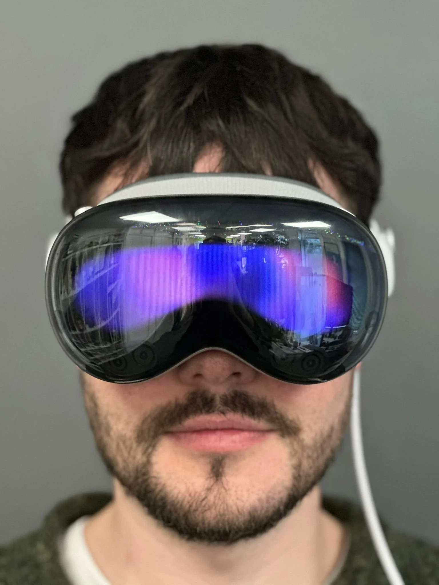 A man with brown hair and a beard wearing a virtual reality headset with reflective lenses showing a purple and blue glow.