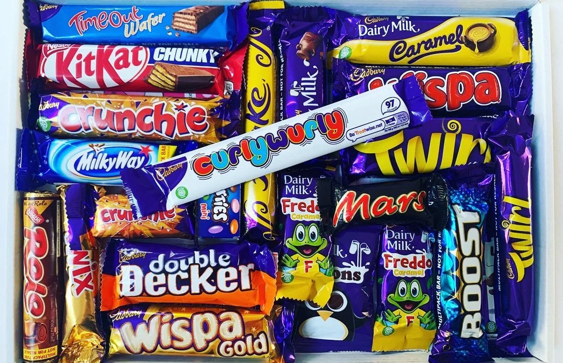 A box filled with assorted chocolate snacks including Kit Kat Chunky, Crunchie, Milky Way, Curly Wurly, Dairy Milk, Twirl, Flake, Double Decker, Wispa Gold, Mars, and several Froddo Frog candies.