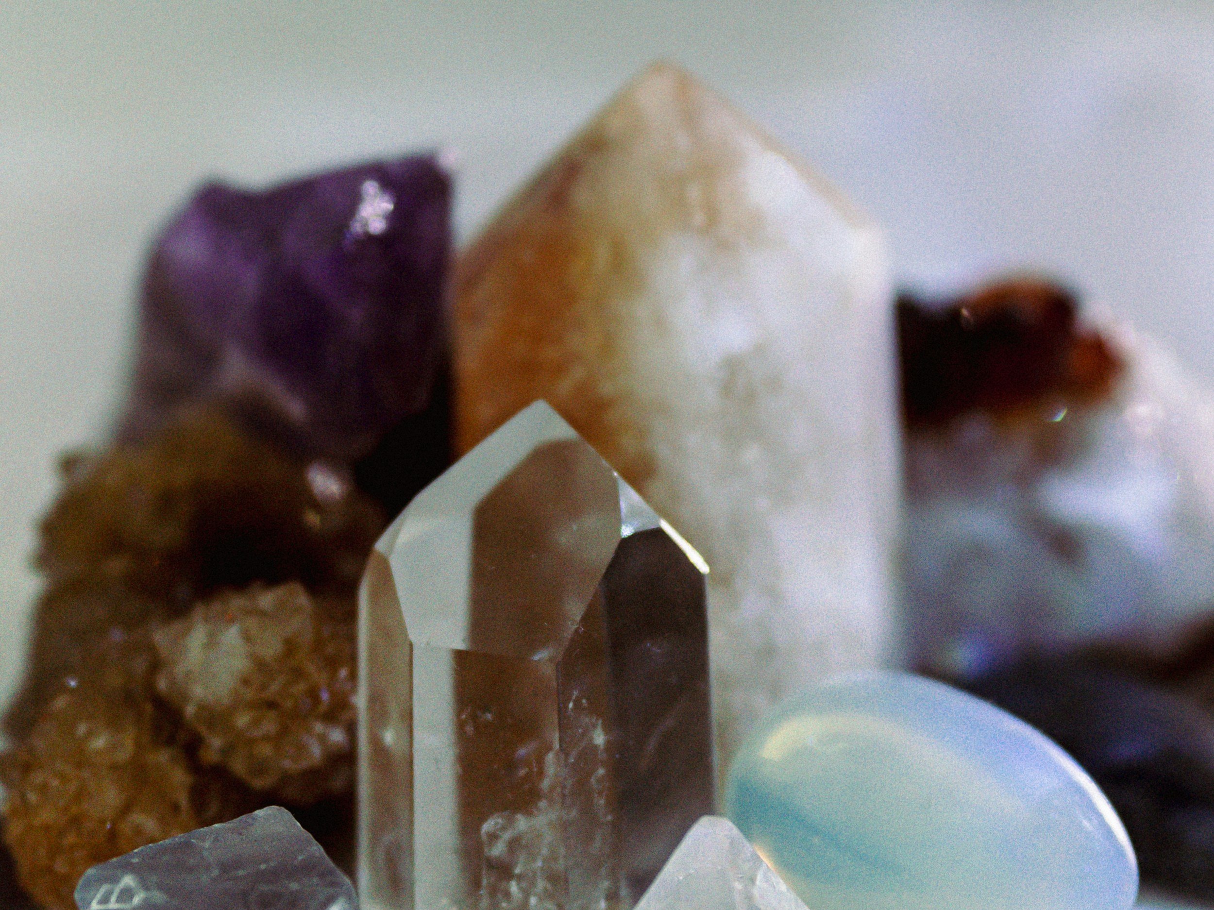 Close-up of various raw gemstones, including purple amethyst, clear quartz, and opal, arranged together.