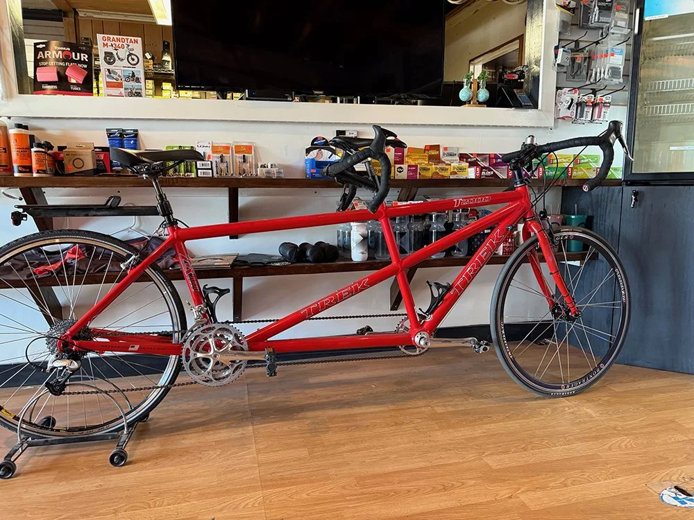 Red Trek road bike with drop handlebars and two water bottle holders, standing on a wooden floor inside a shop.