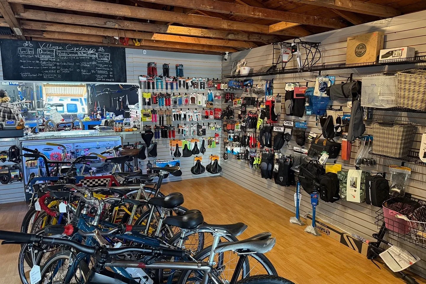 Interior of a bicycle shop with bikes on display, shelves of bike accessories, and tools, with a chalkboard menu on the wall.