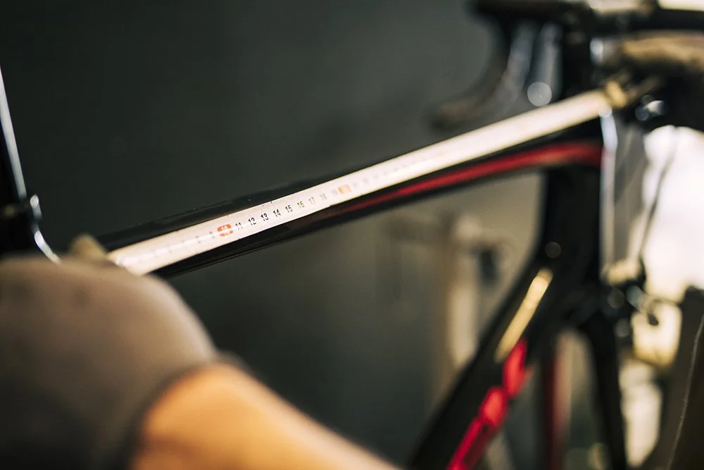Close-up of a black bicycle frame with a white and red top tube, with a blurred background.