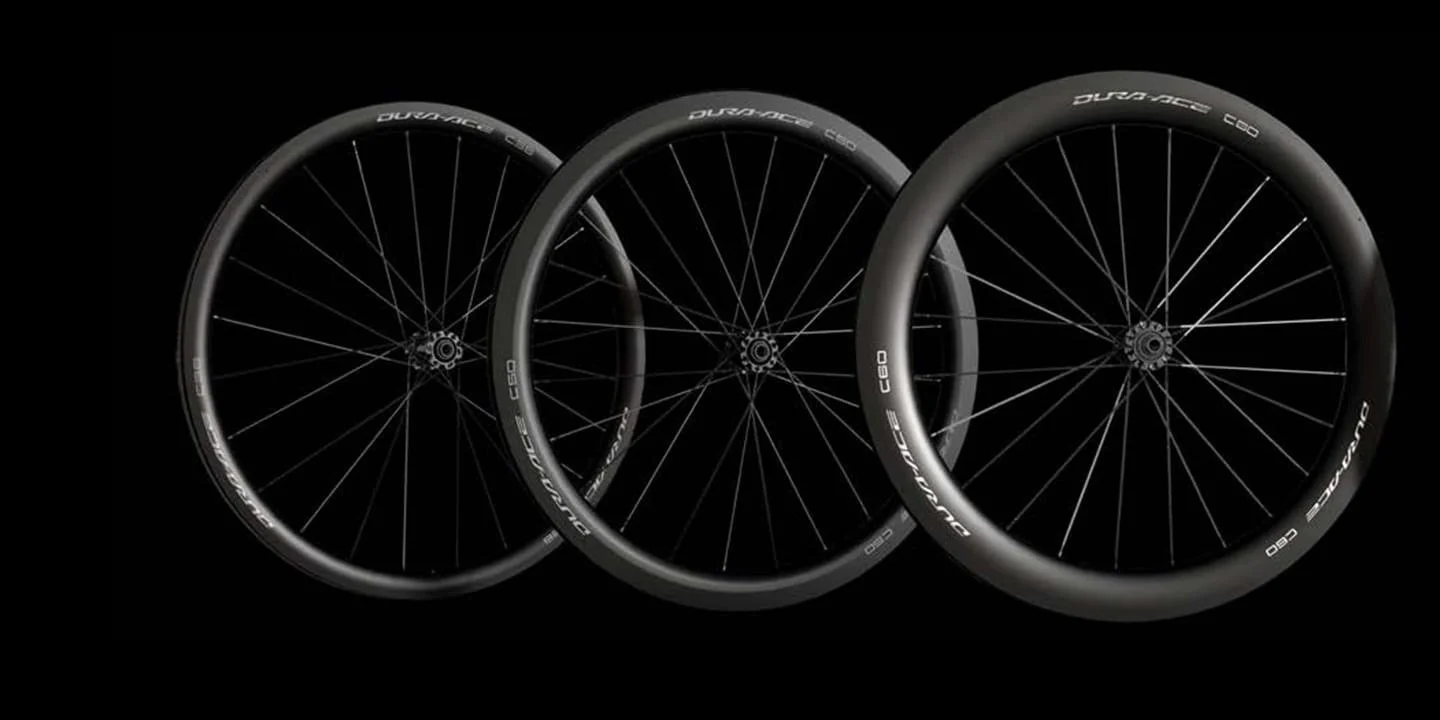 Three black bicycle wheels with spokes and labeled with 'DURA-ACE' and 'C60,' arranged in a diagonal line against a black background.