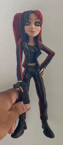 Hand holding a figurine of a woman with long black and red hair, dressed in a black leather outfit.