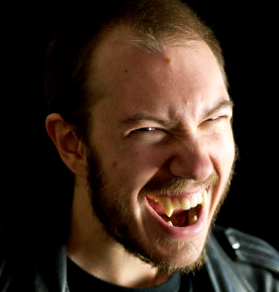Close-up of a man with long hair and beard, laughing passionately, wearing a black leather jacket.