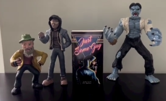 Three monster figurines and a 'Just Some Guy' card on a black surface against a beige wall.