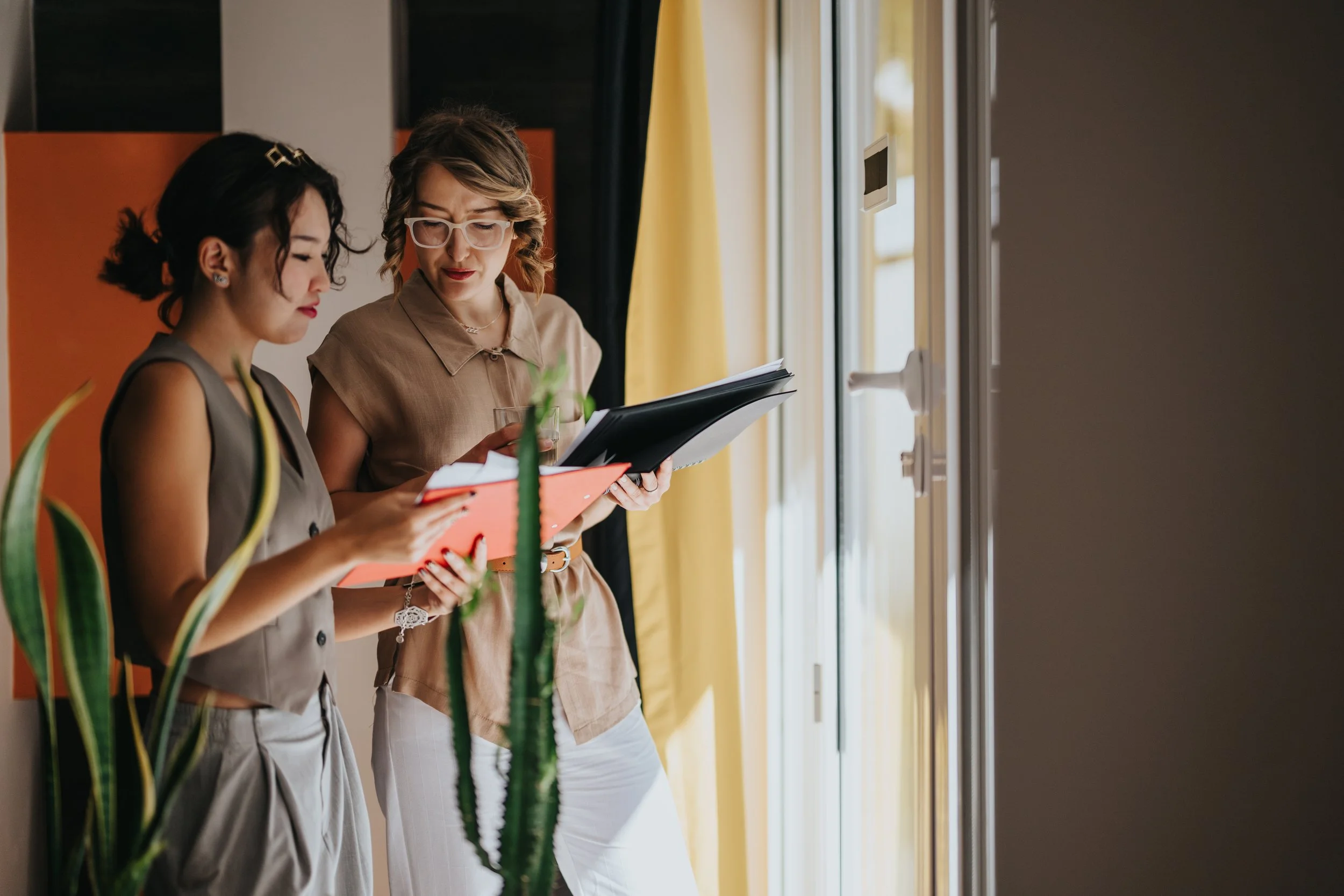 A woman business owner standing with a female Certified Exit Planning Advisor, sharing documents on paper and a tablet. They are analyzing the company's valuation to determine next steps for growing or selling the business.