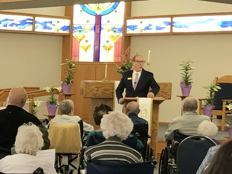 Chaplain Noel speaking at a podium in the Chapel of the Good Shepherd at St. John's Circle of Care in Brown County Minnesota