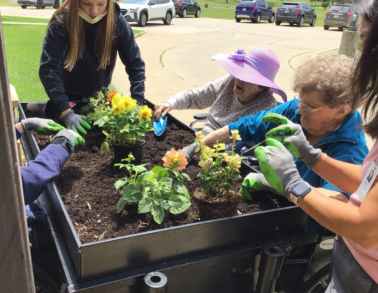 Volunteers and residents planting flowers in a raised flower bed at St. John's Circle of Care in Springfield MN