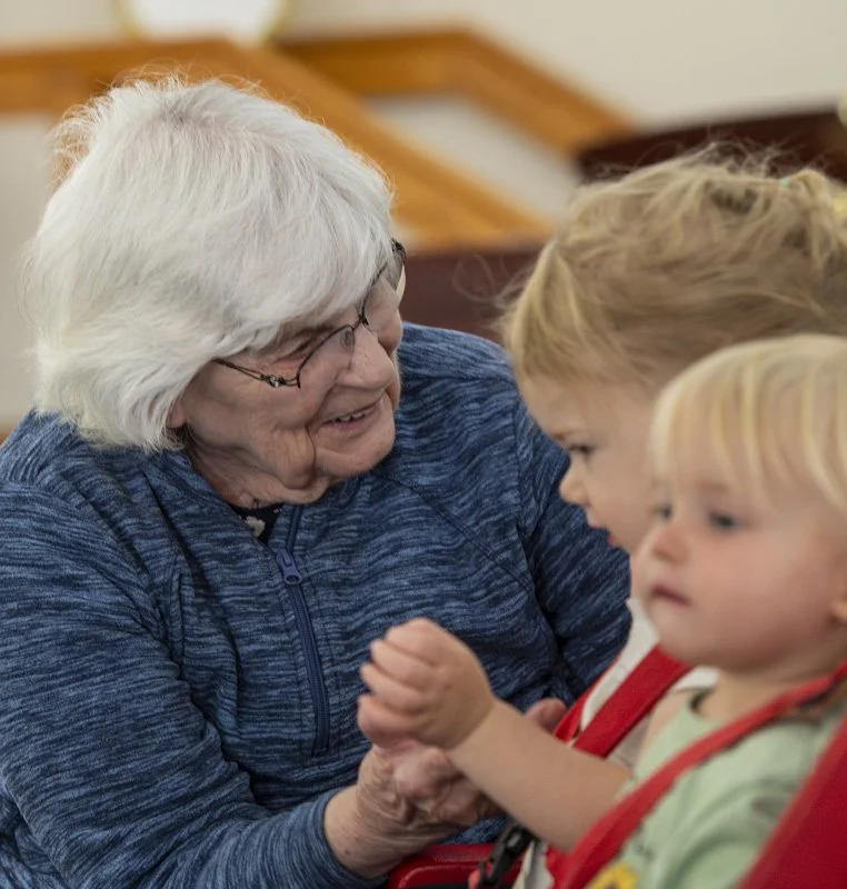 A resident of St. John's smiling as she interacts with two young children from Grandkids Daycare Center