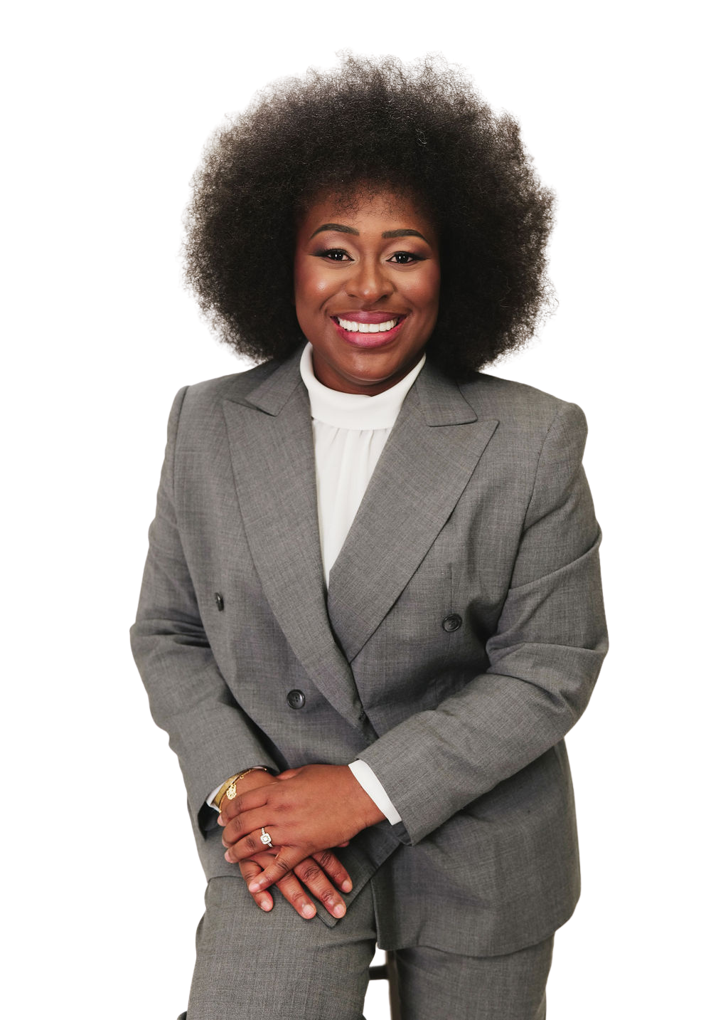 African American woman in a gray business suit smiling, standing with hands clasped in front, white blouse, dark curly hair, and gold jewelry.