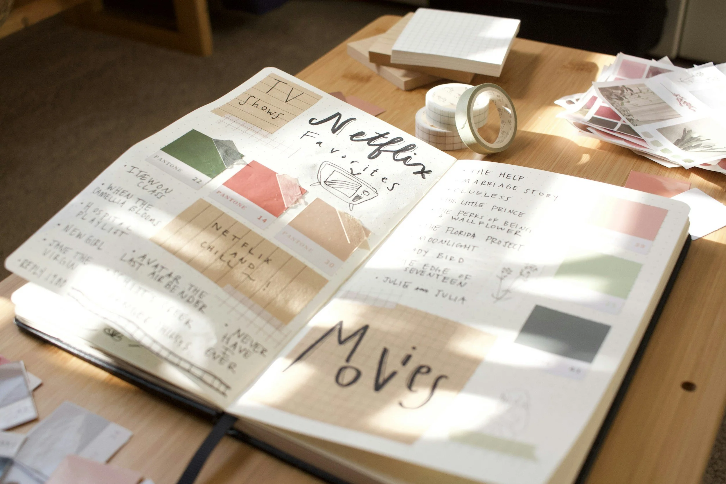 A wooden table with various scrapbooking supplies including patterned papers, washi tape, and an open scrapbook with handwritten notes and photos.