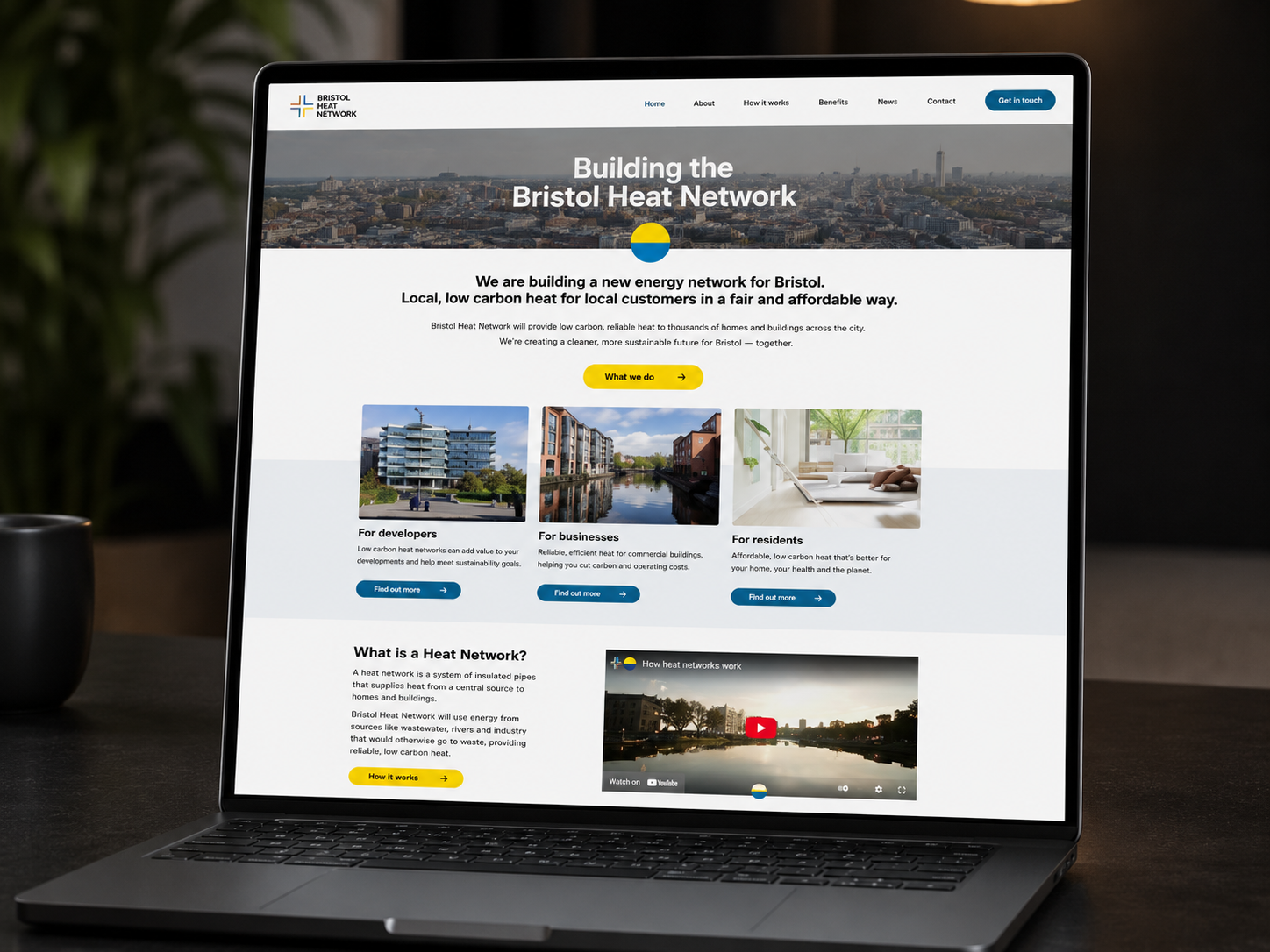 Laptop screen displaying the homepage of the Bristol Heat Network website, featuring information about building a low-carbon energy network for Bristol, with sections for developers, businesses, and residents, and a video at the bottom.