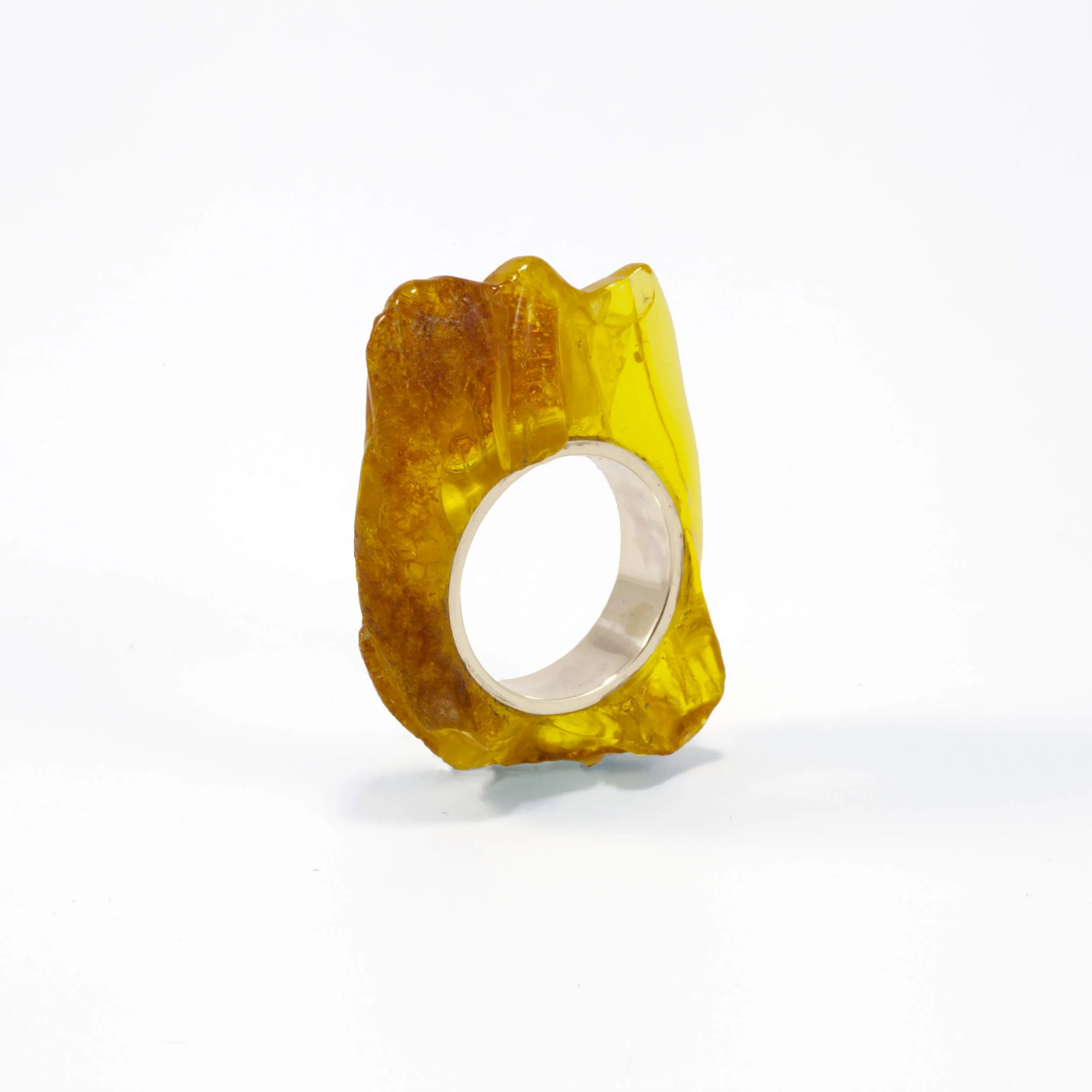 A ring made from a large, irregularly shaped amber stone with a silver band setting, displayed against a white background.