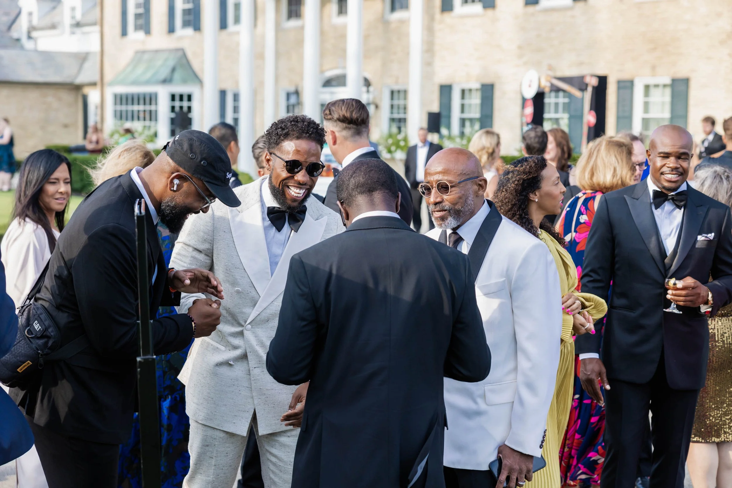 A group of people dressed in formal attire at an outdoor event, engaging in conversations and smiling.