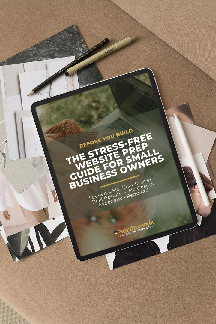 Tablet displaying a guide for small business owners with the title 'Before you build: The stress-free website prep guide for small business owners'. The tablet is on a table surrounded by photographs, notebooks, and pens.