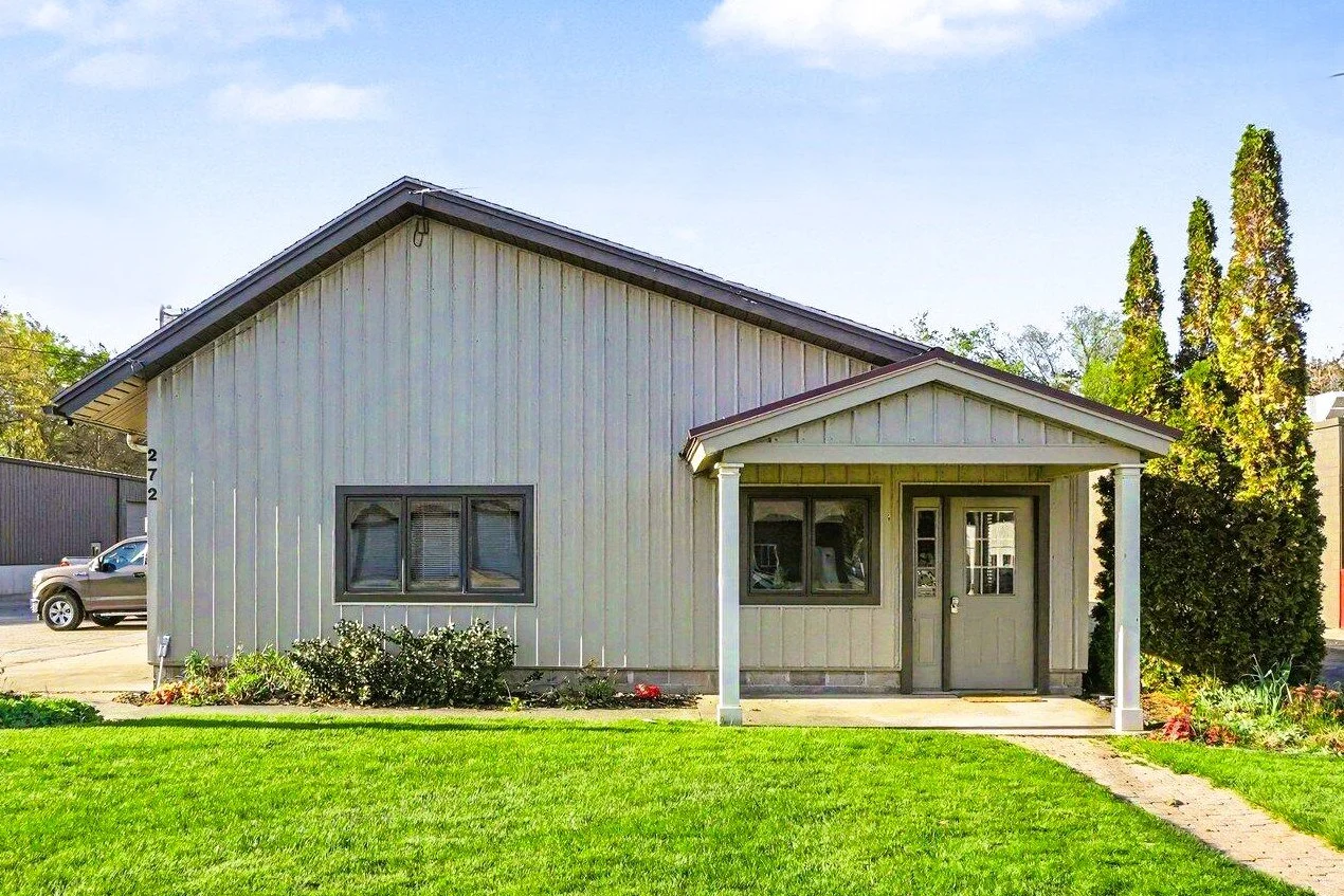 A house with a gray exterior, a small front porch with columns, and a manicured green lawn.
