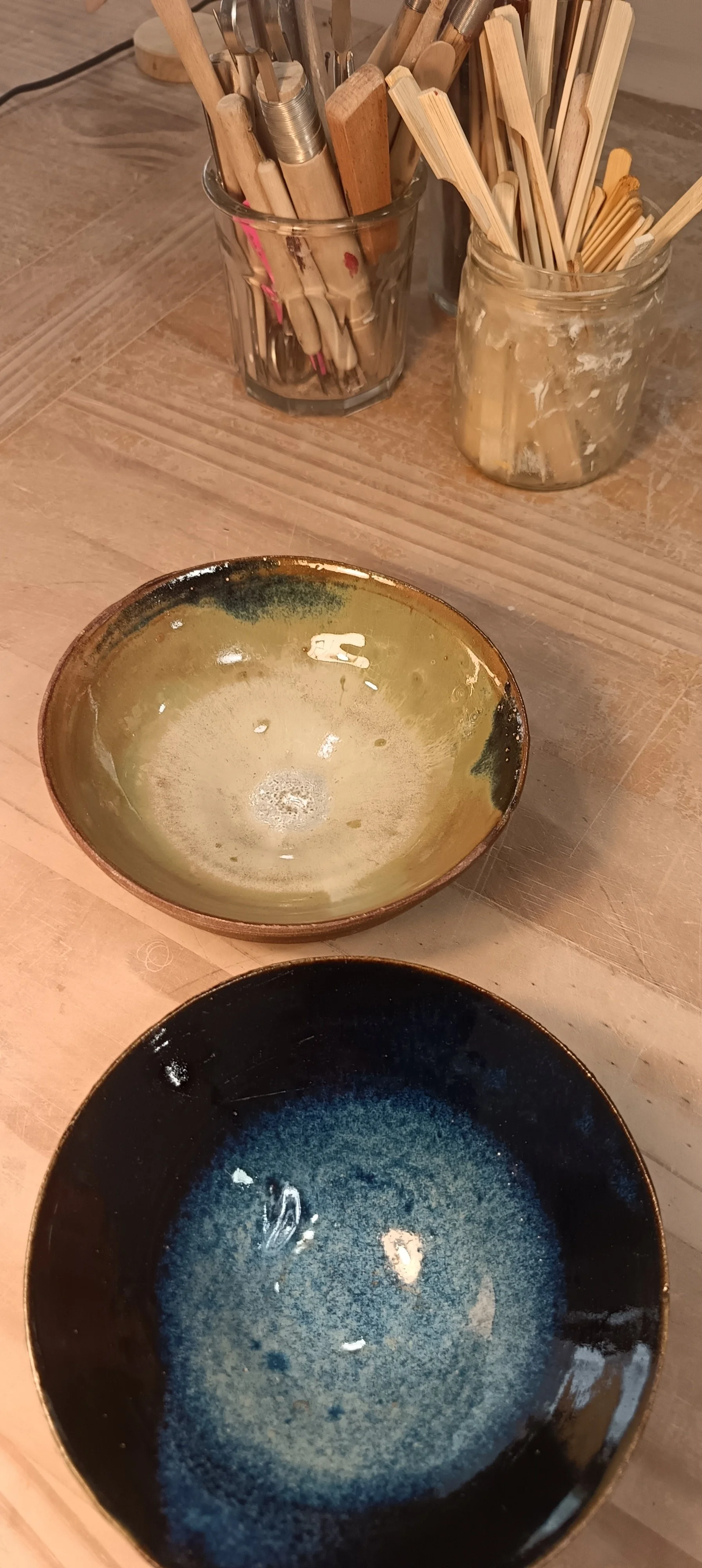 Assiettes en céramique de différentes couleurs sur une table en bois, et bacs en verre contenant des ustensiles en bois.