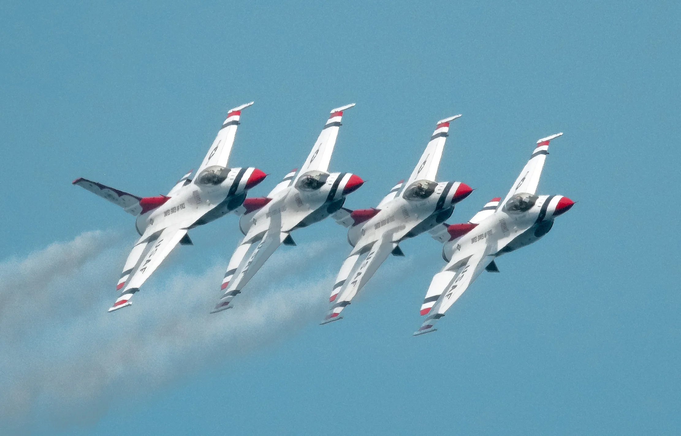 Four fighter jets flying in close formation in a clear blue sky.