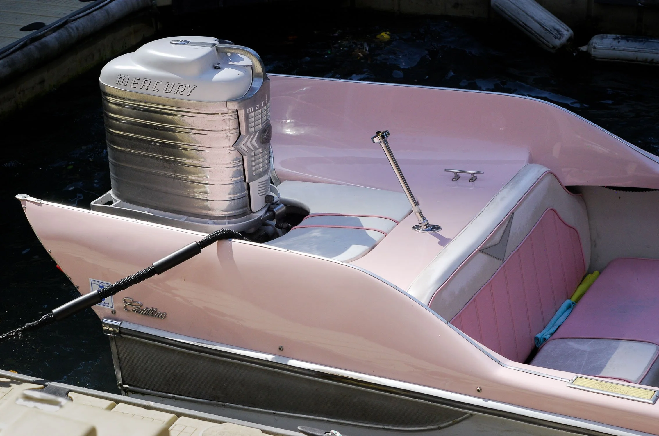 A pink Cadillac boat with a Mercury outboard motor docked at a pier.