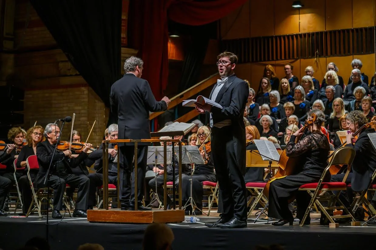 An orchestra performing on stage with a conductor and a male singer in a tuxedo singing.