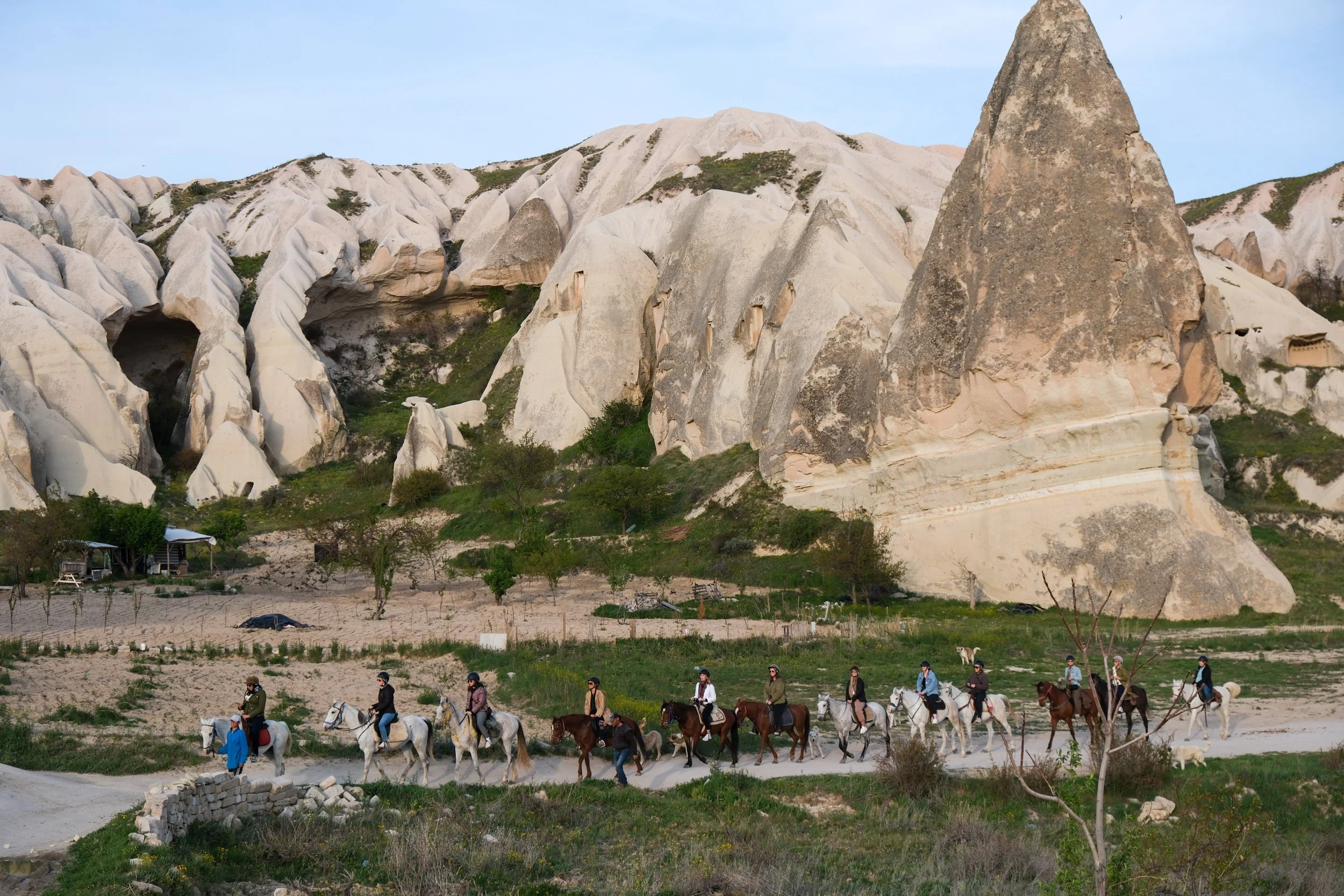 Tourists riding horses in a valley with unique rock formations and caves in the background