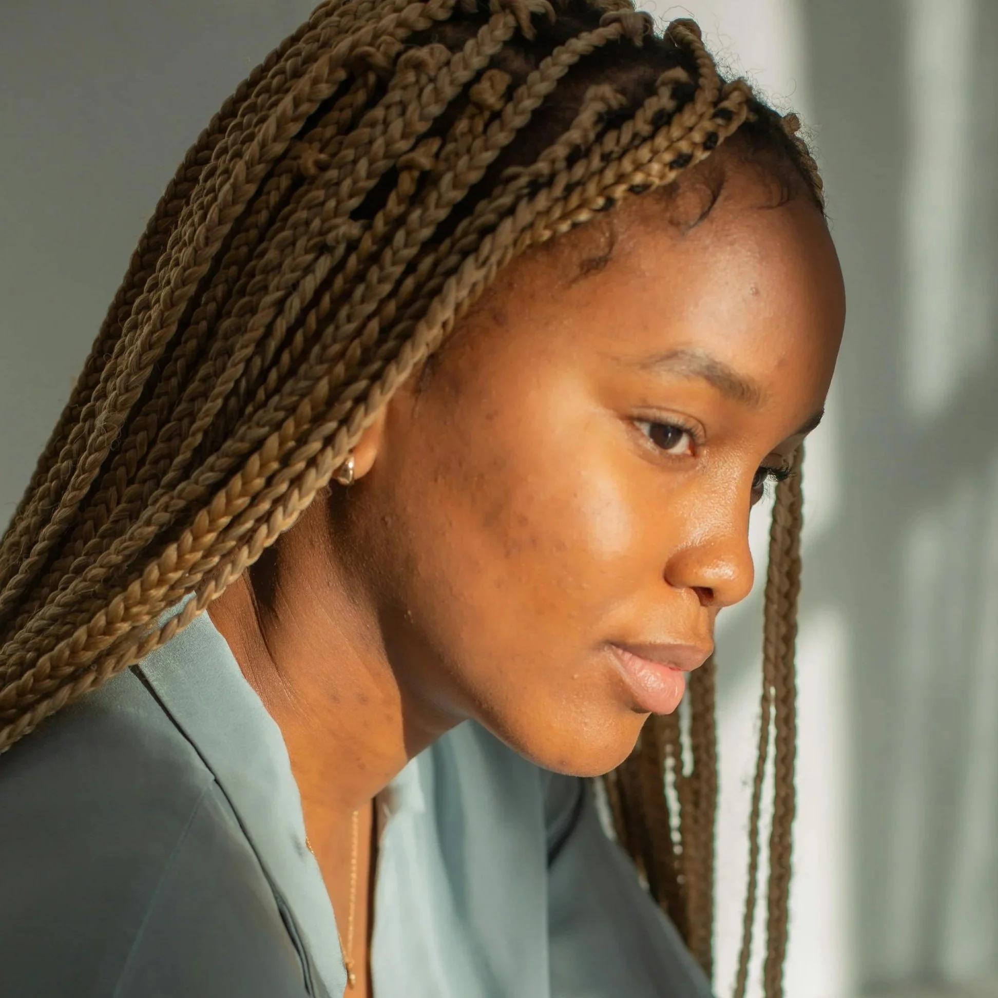 A woman with long braided hair looking down thoughtfully.