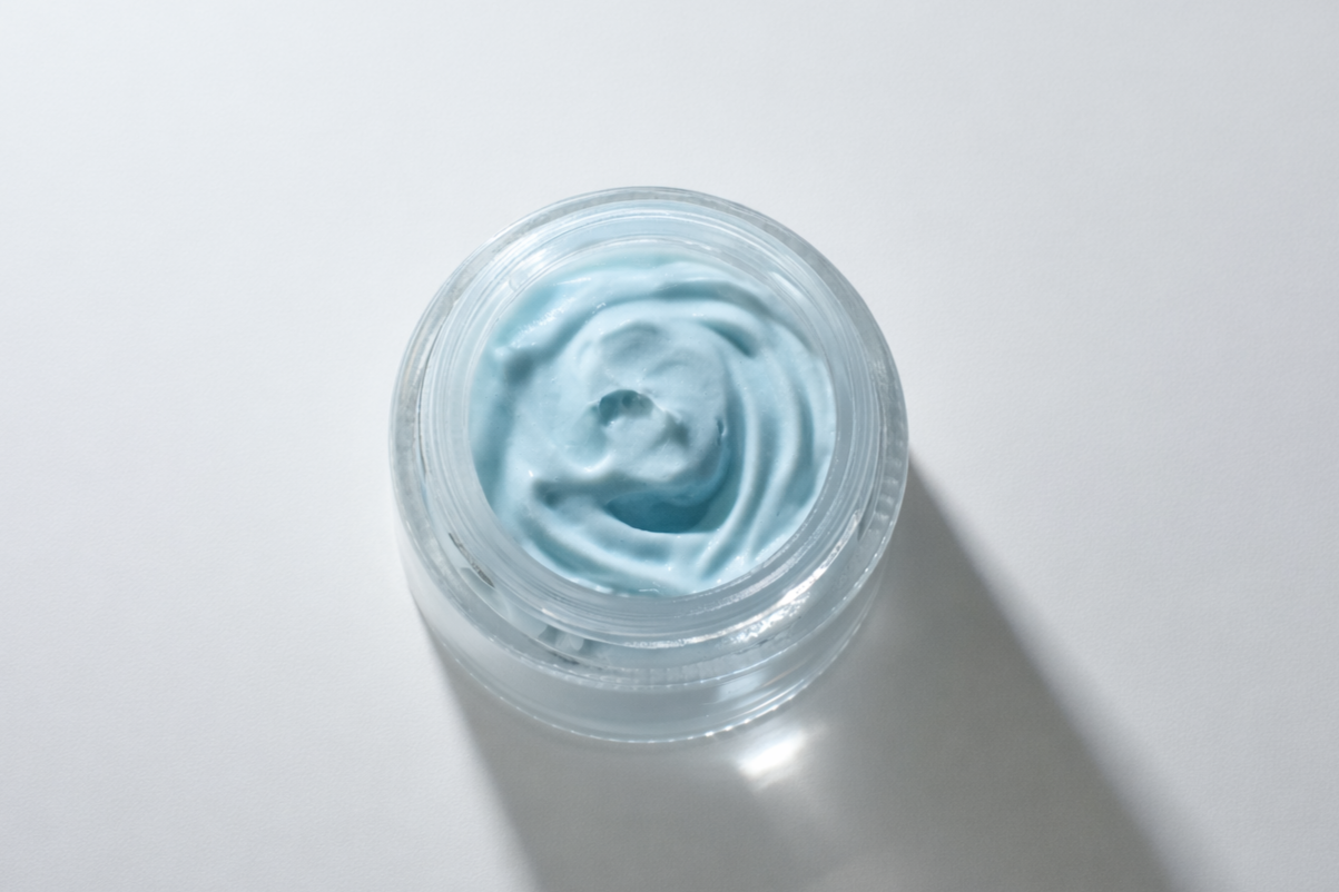 Open container with light blue cream or gel on a white surface.